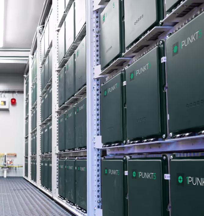 Rows of black storage or battery units labeled 'PUNKT5' mounted on white industrial shelves inside a clean facility.