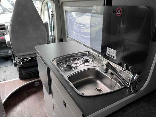 Innenansicht eines Wohnmobils mit kleiner Küche, ausgestattet mit einem Herd mit zwei Flammen und einer Spüle.