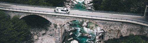 Familie sitzt und steht neben einem Wohnmobil auf einer Rasenfläche mit Bäumen im Hintergrund.