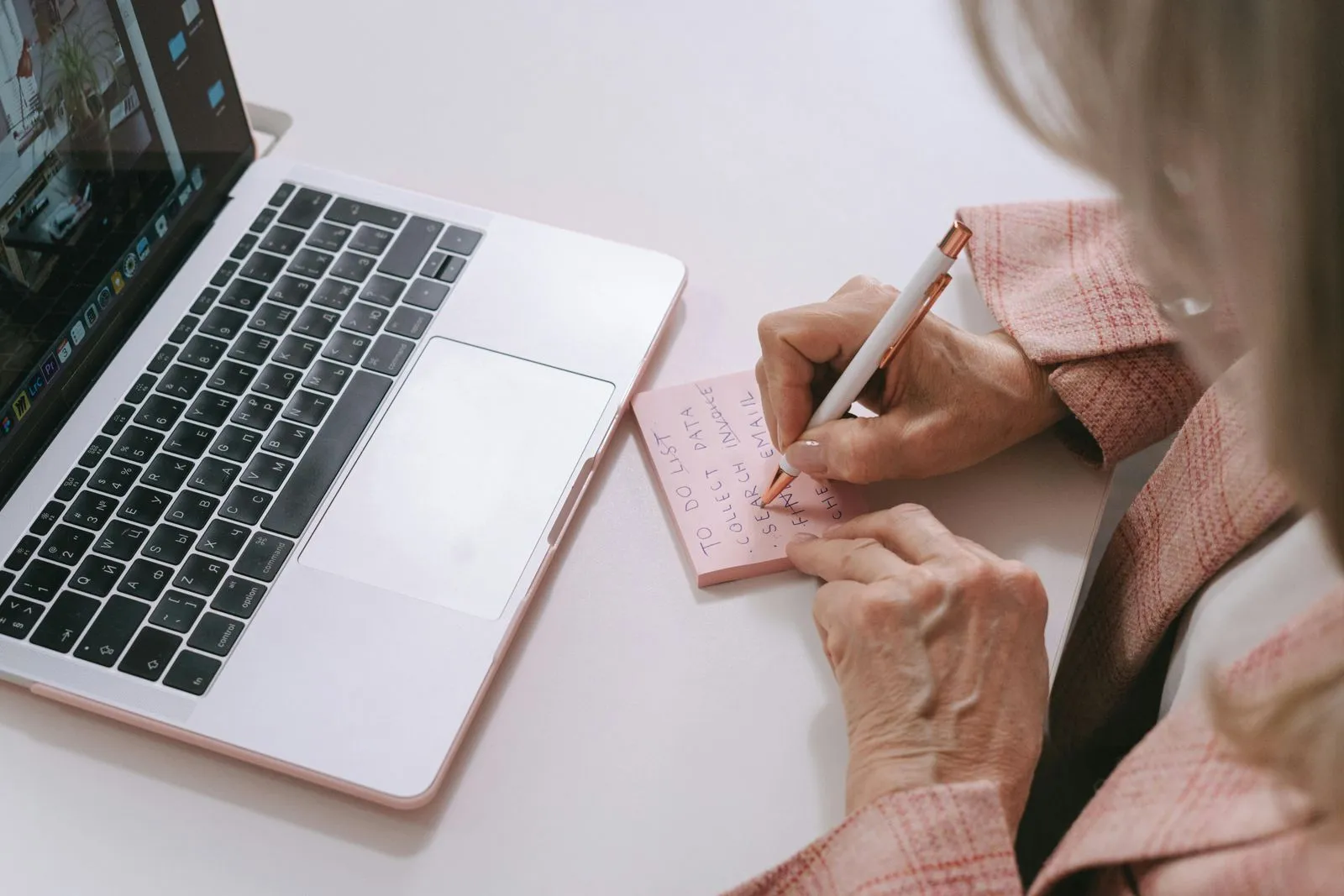 A person holding a pen and writing on a post-it in front of the computer