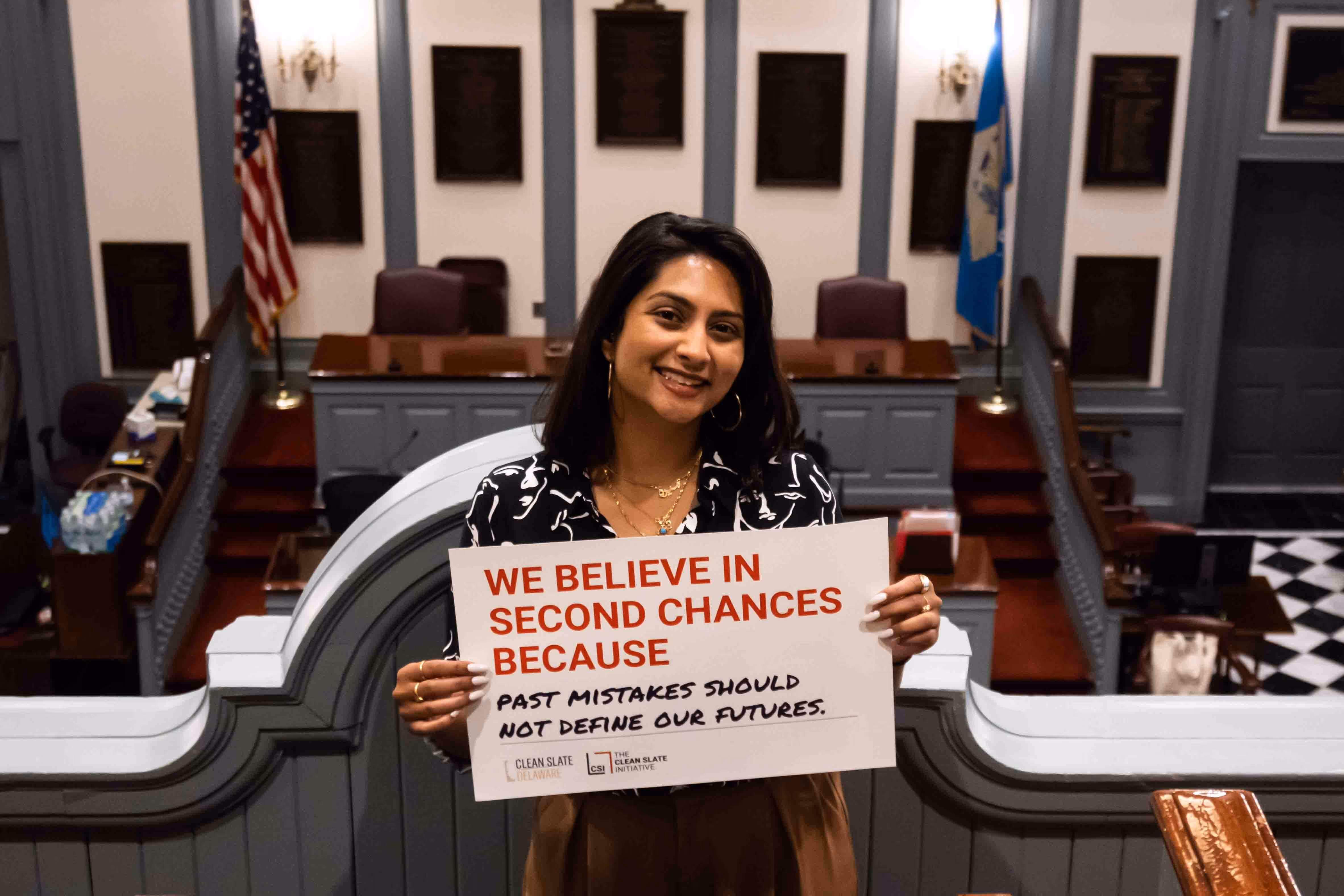A woman holding a sign that says "We believe in second chances because past mistakes should not define our futures.".