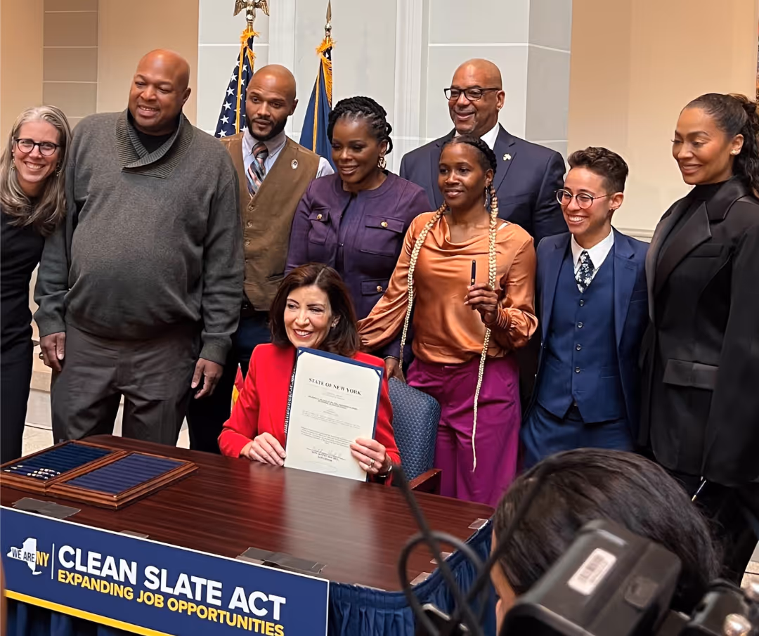 A group of people are standing around a table with a woman holding a document.