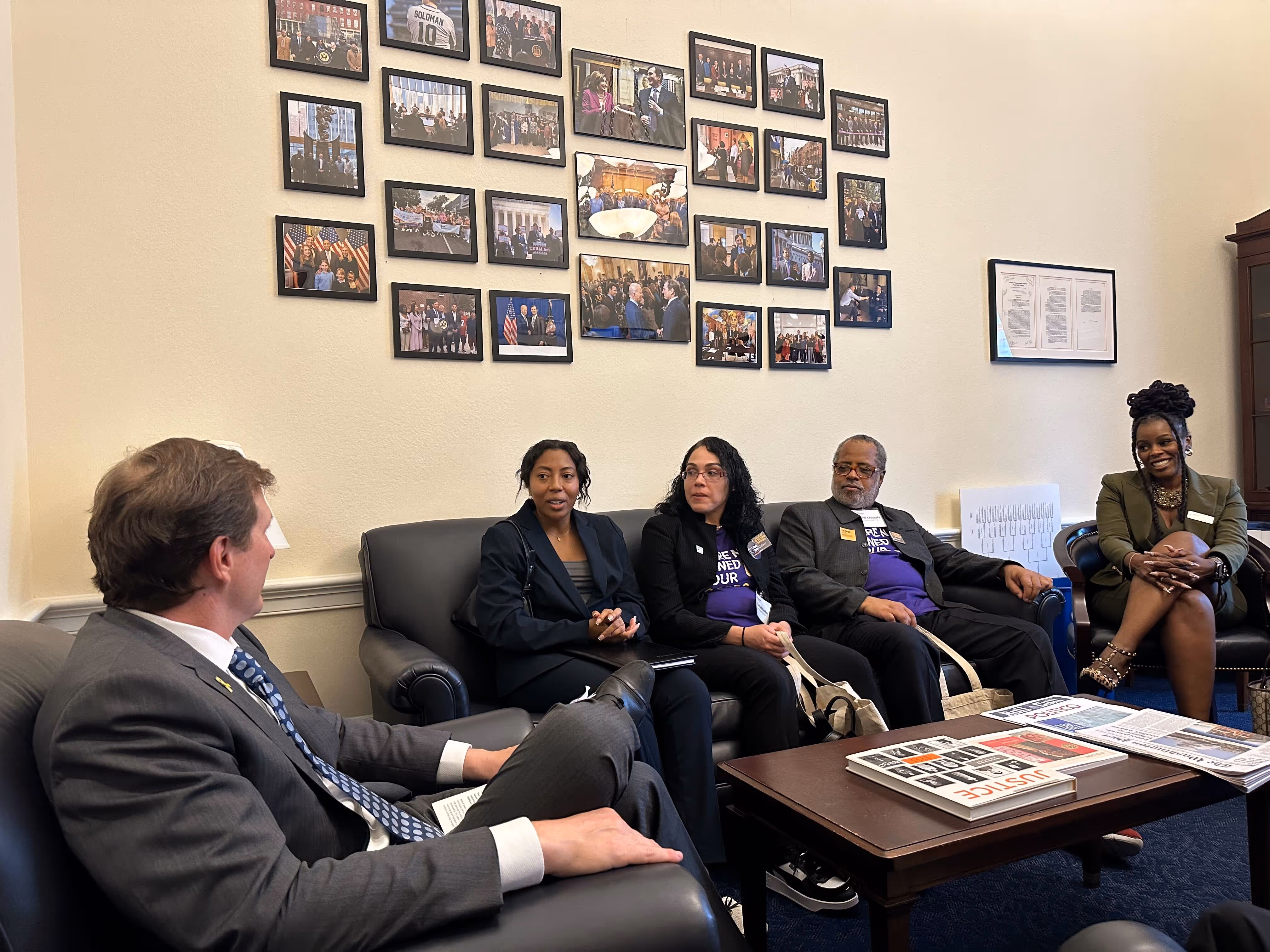 A group of people sitting in a room with a black and white photo of a congressman on the wall.