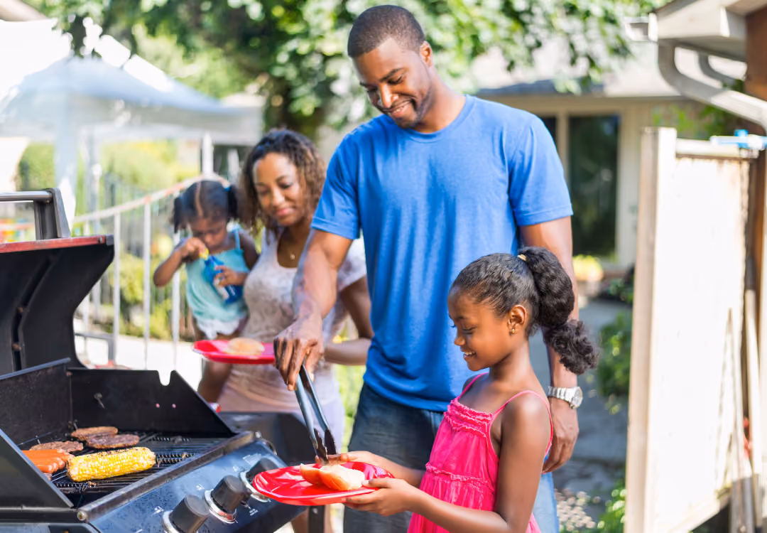 Happy family of four standing outside grilling dinner: mother, father, and two young daughters