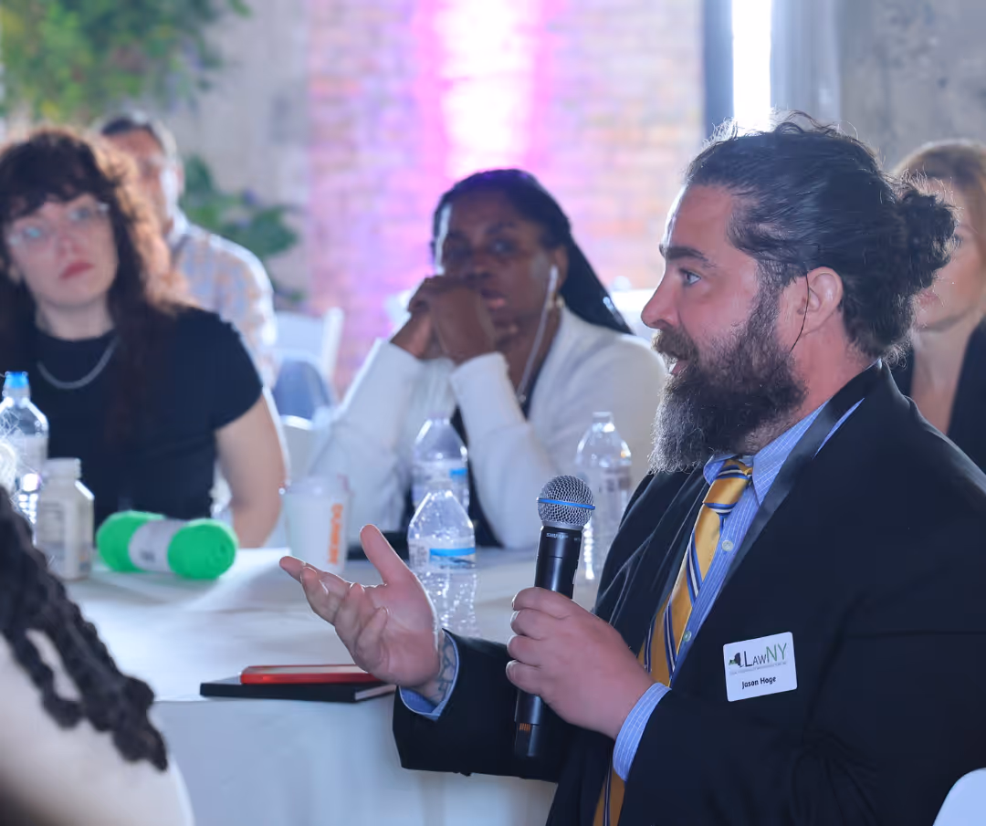 A man with a beard and a yellow tie speaks into a microphone.