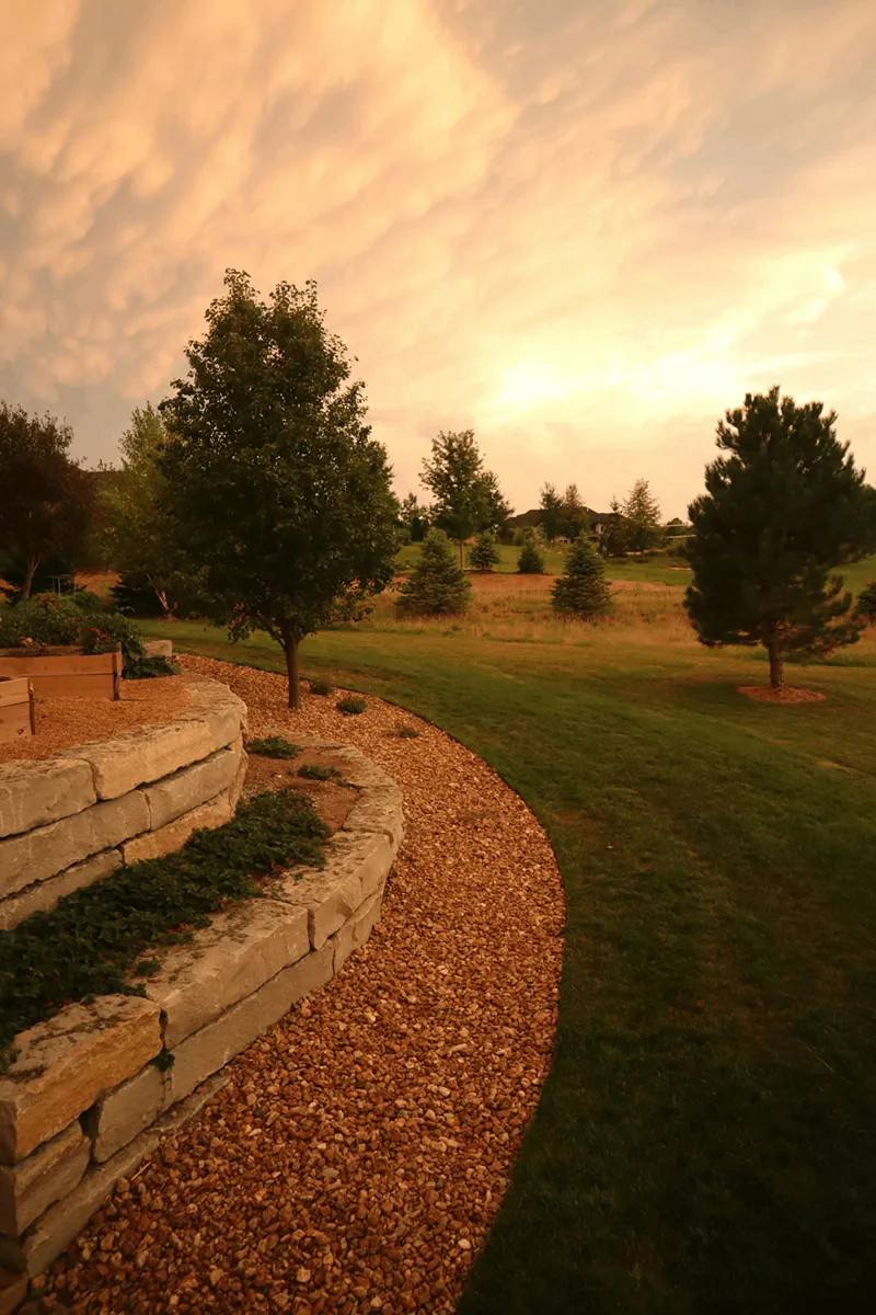 Garten mit Natursteinmauer, Hochbeet und Rasenfläche bei Sonnenuntergang – Symbol für individuelle Hang- und Landschaftsgestaltung durch Daniel Lasser Gartenbau