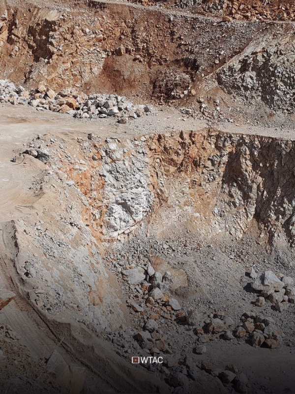 A large open-pit mine with exposed earth layers and scattered rocks, showing terraced excavation and rugged terrain.