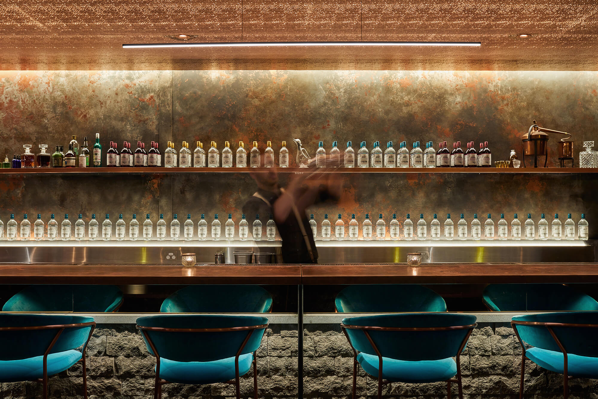 Raw Stone Front Teal Velvet Seats Patinated Wall Backlit Bottle Ledge Linear Lighting Bronze Ceiling in Naught Distilling. Photo by Graham Denholm.