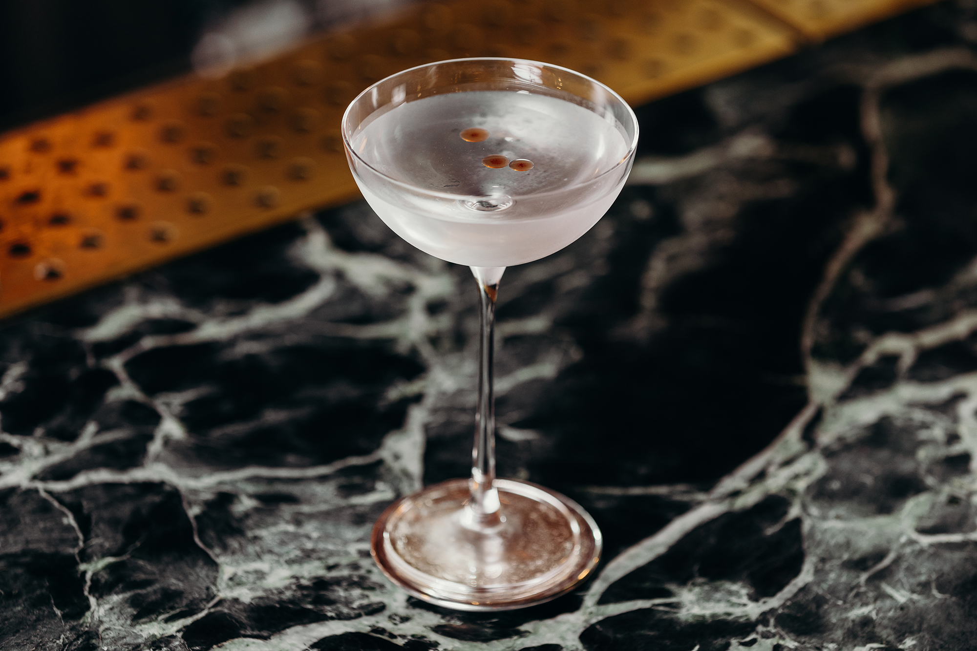 Elegant Martini Coupe Glass Verde Green Marble Bar Top Perforated Brass Drip Tray Garnish Detail in Nick & Nora’s. Photo by Ryan Sauer.