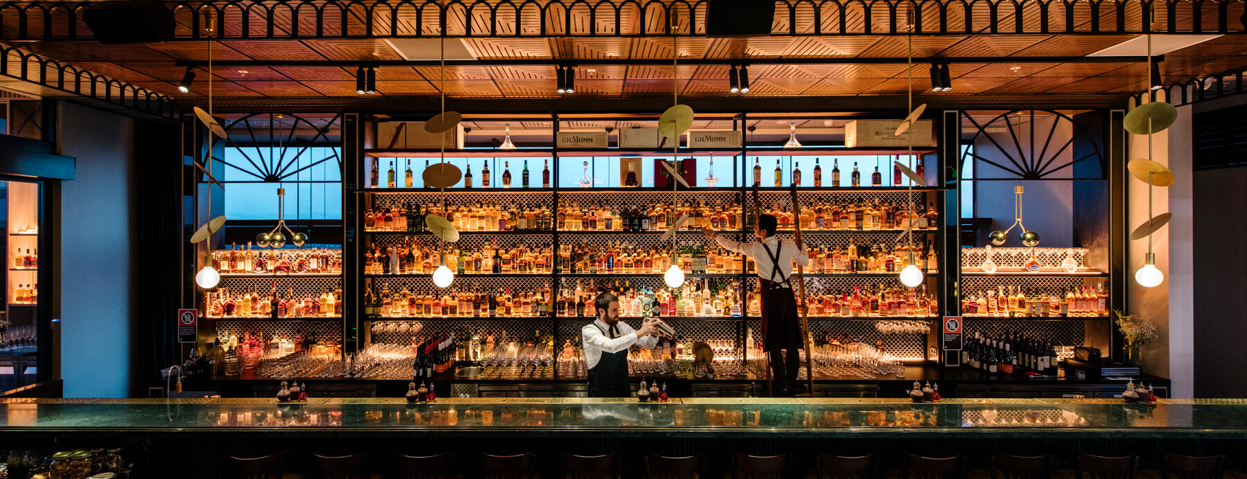 Emerald Stone Bar Backlit Spirit Library Gold Disc Pendants Timber Panelled Ceiling Scalloped Tile Backsplash in Nick & Nora’s. Photo by Ryan Sauer.