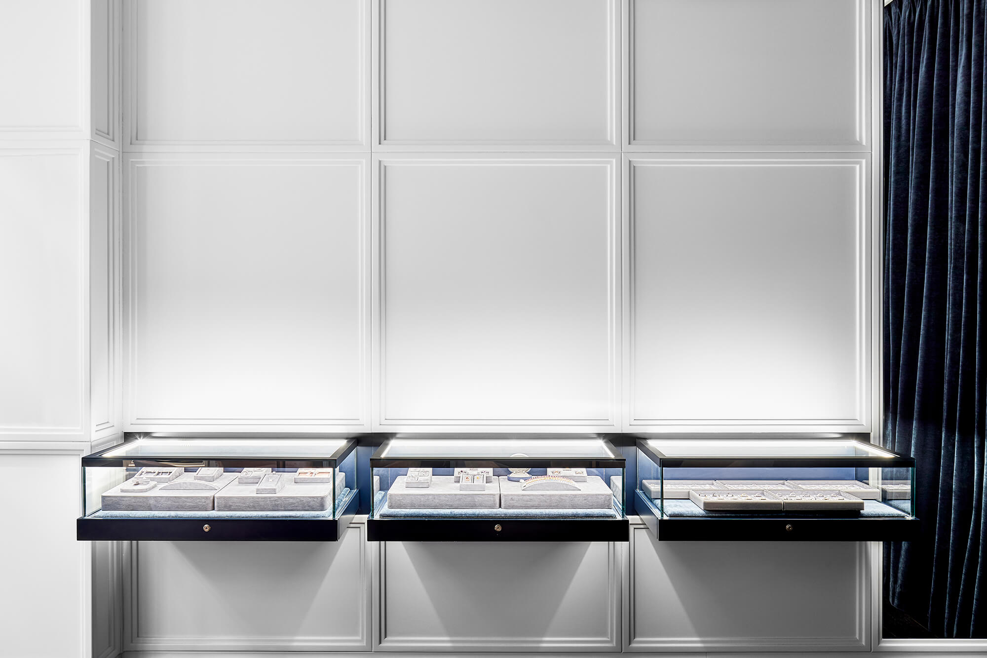 Cantilevered Glass Showcases Integrated LED Lighting White Panel Wall Moulding Navy Velvet Drapery Minimalist Retail Design in Reigne Jewellery. Photo by Nicole Reed.