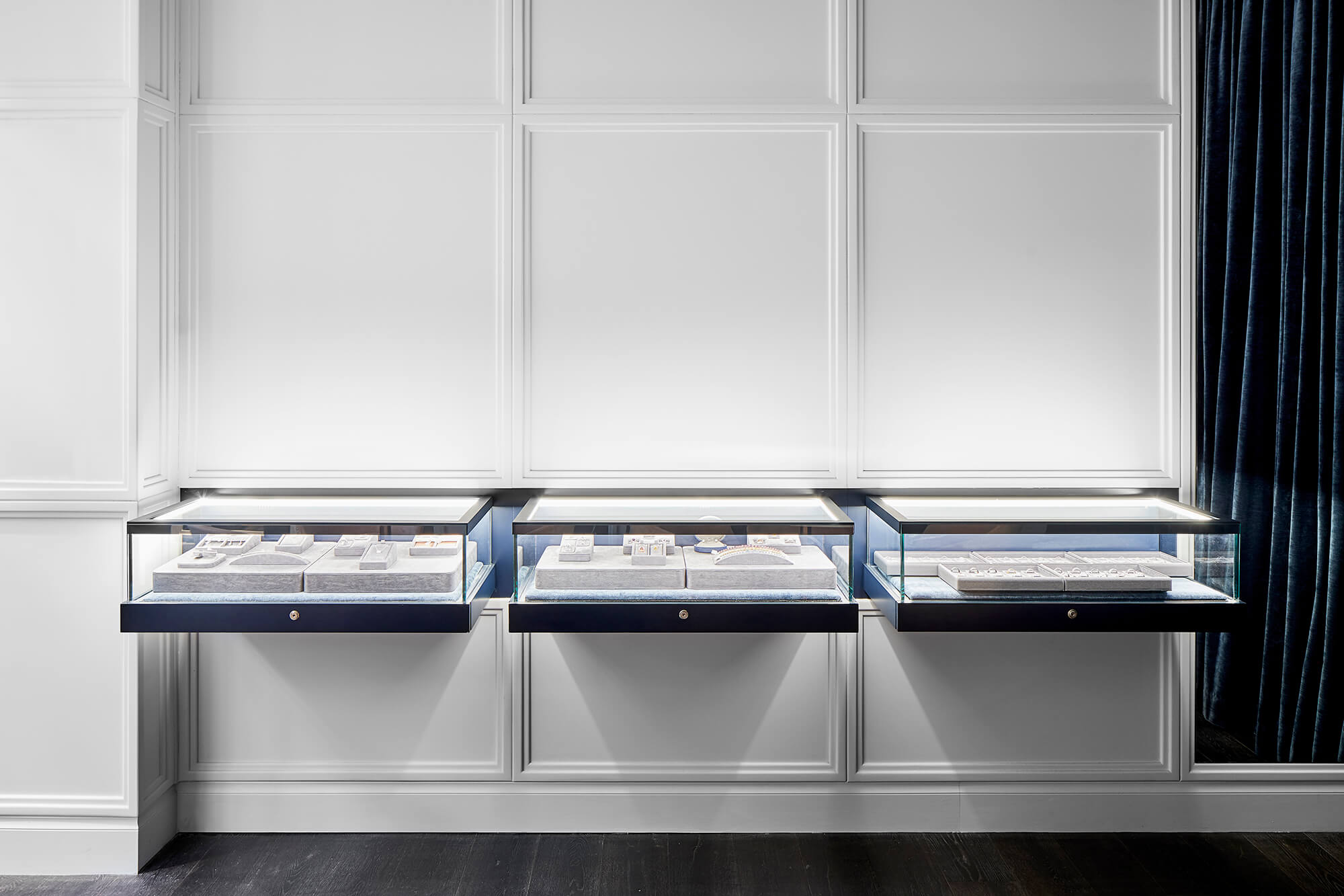Trio of Floating Glass Vitrines Internal LED Illumination White Neoclassical Wall Panelling Navy Velvet Accents Dark Oak Floors in Reigne Jewellery. Photo by Nicole Reed.