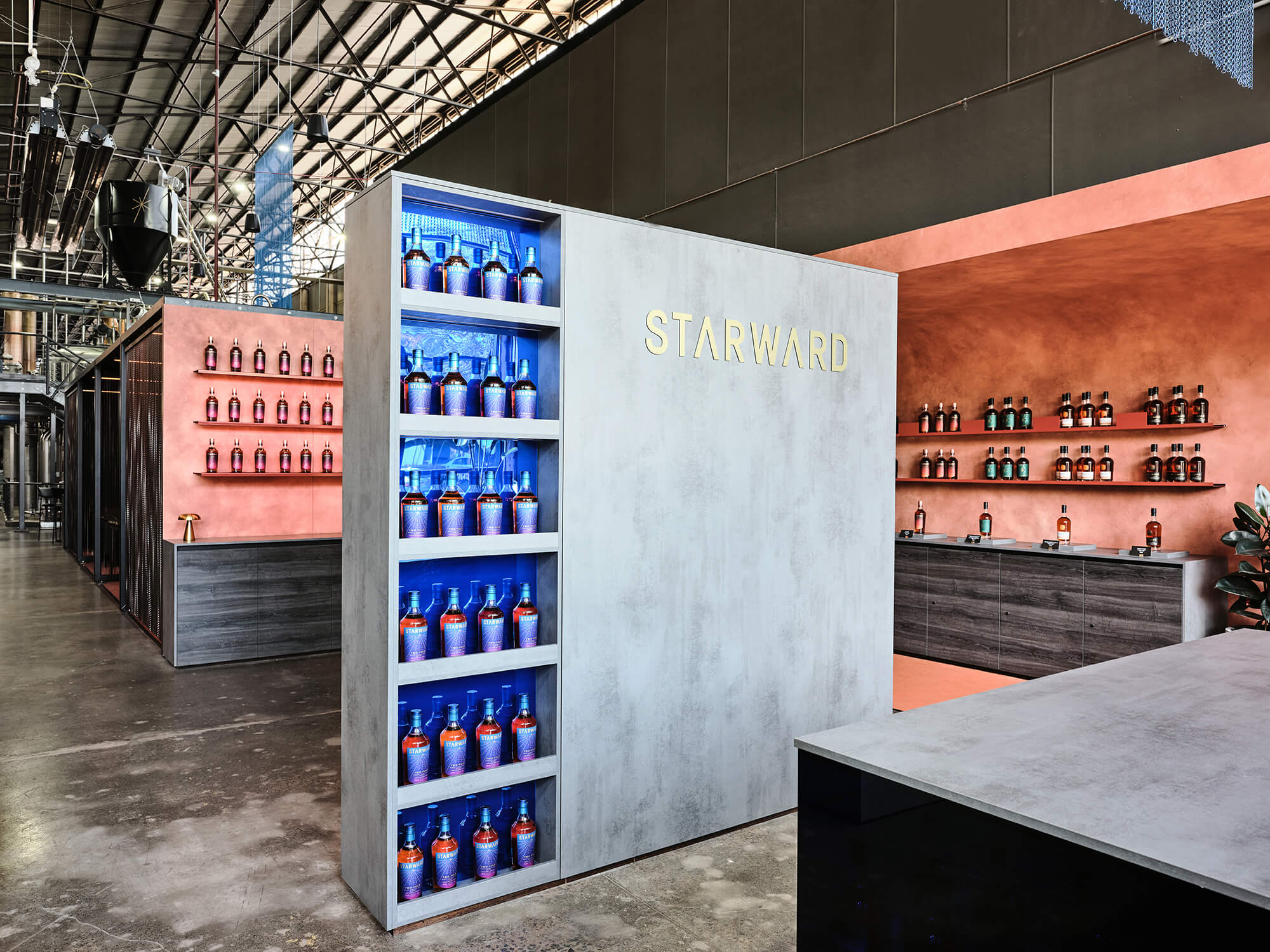 Concrete-Look Partition Backlit Blue Bottle Display Gold Brand Signage Terracotta Rendered Walls Industrial Distillery Setting in Starward. Photo by James Geer.