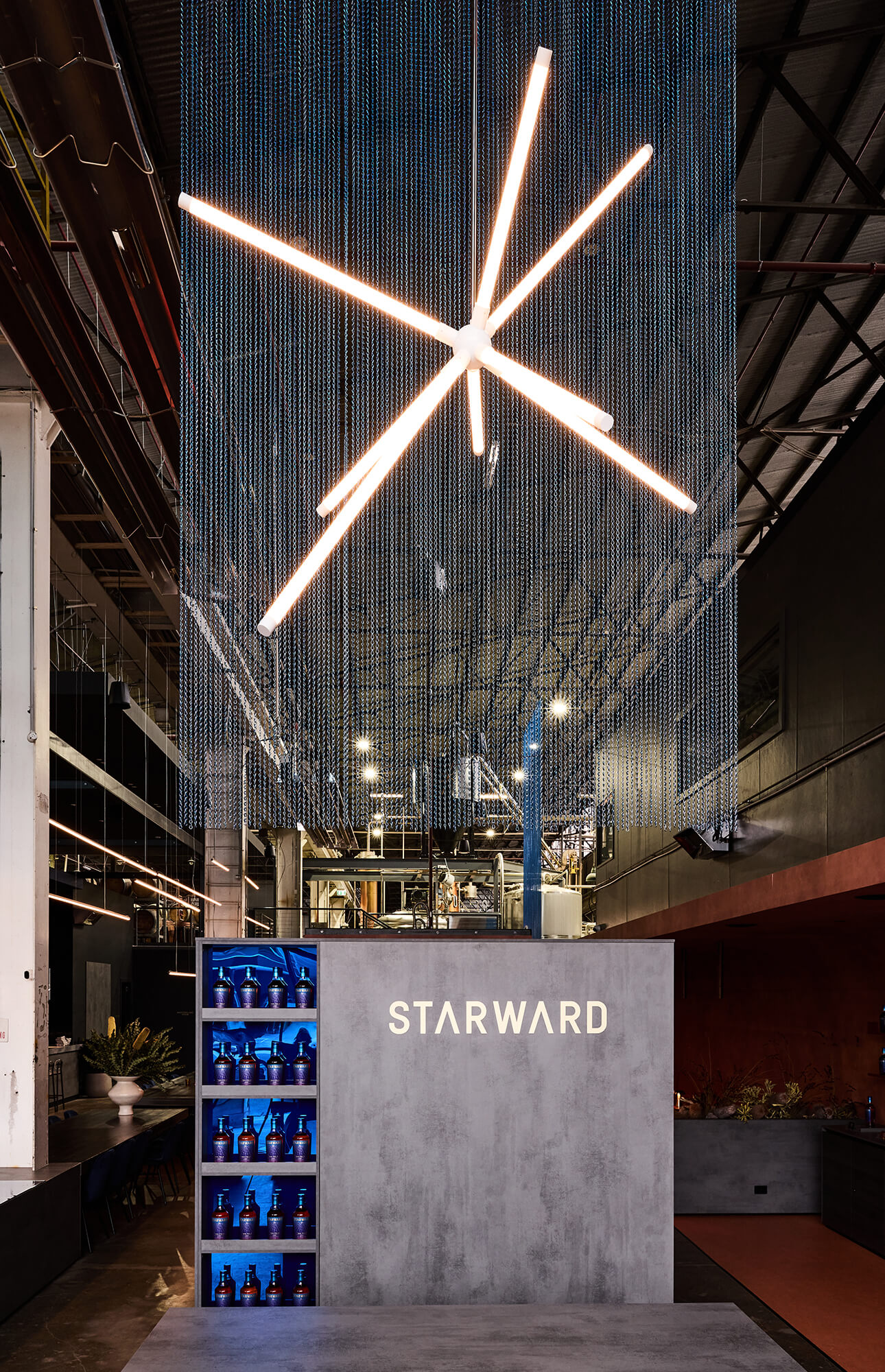 Radiating Starburst Light Fitting Shimmering Chainmail Backdrop Concrete-Textured Joinery Blue Backlit Shelving Industrial Warehouse Scale in Starward. Photo by James Geer.