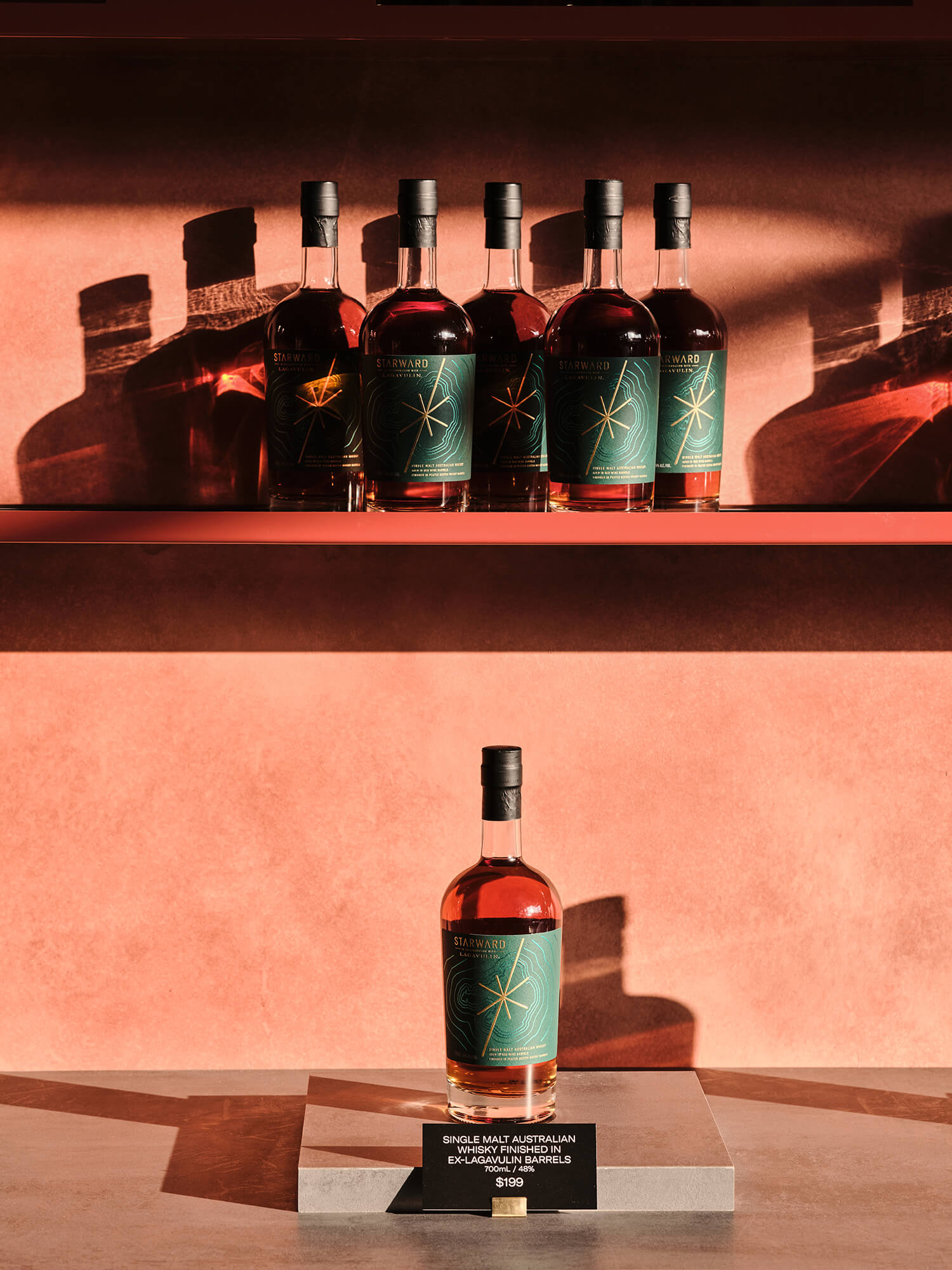 Single Malt Australian Whisky Curation Minimalist Red Floating Shelf Terracotta Stucco Wall Dramatic Sunlight Shadows Stone Plinth in Starward. Photo by James Geer.