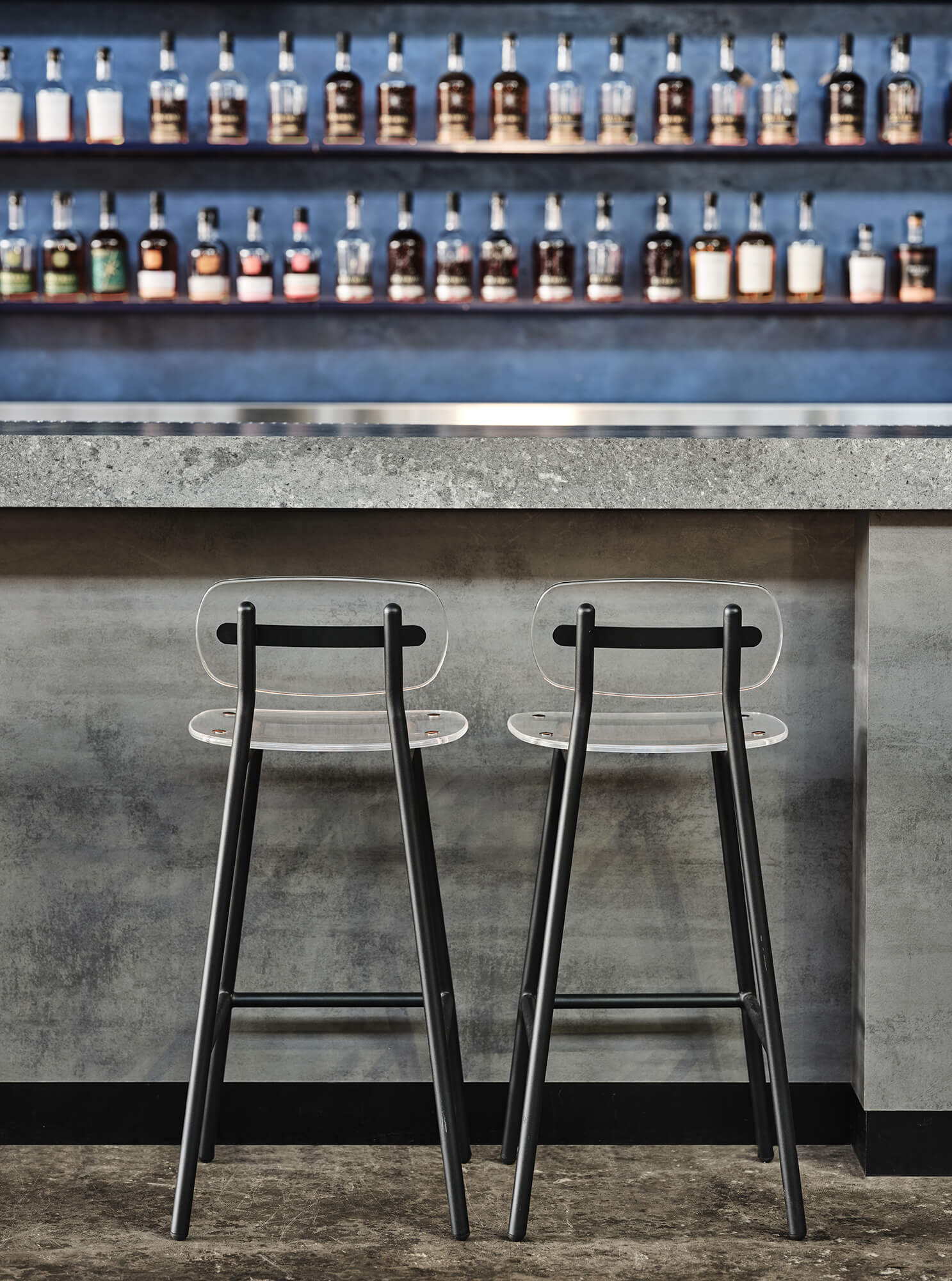 Cast Concrete Bar Counter Clear Acrylic Stools Black Steel Frames Recessed Blue Backlit Spirit Shelving Minimalist Distillery Interior in Starward. Photo by James Geer.