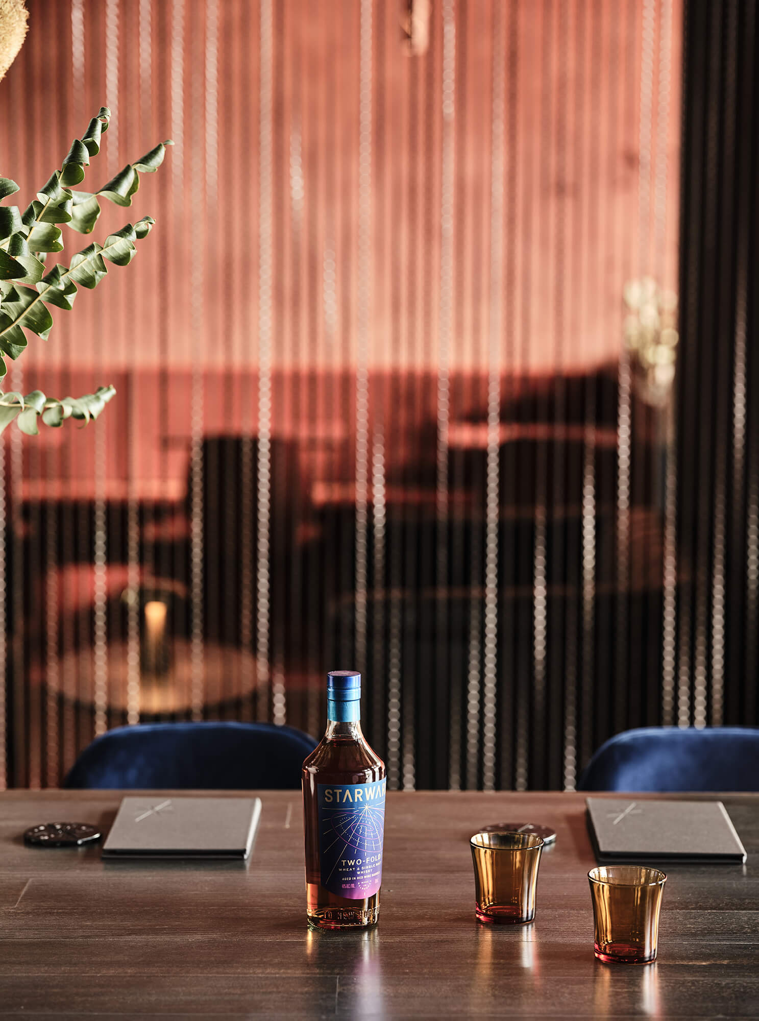 Dark Timber Tabletop Amber Glassware Blue Velvet Chairs Metal Chain Curtain Backdrop Warm Glowing Ambiance Starward Whisky Service in Starward. Photo by James Geer.