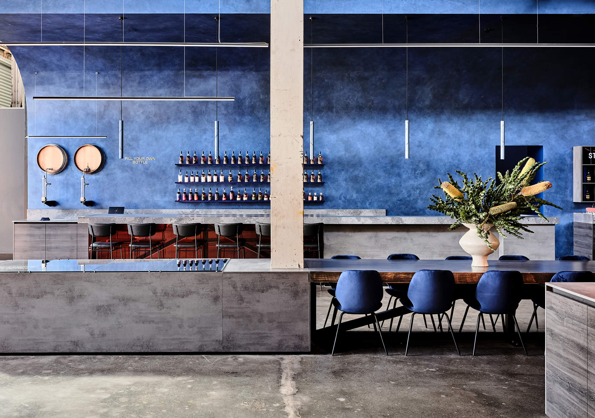 Deep Azure Textured Walls Arched Ceiling Profile Concrete-Look Counter Blue Velvet Dining Chairs Linear LED Pendants Distillery Bar Scene in Starward. Photo by James Geer.