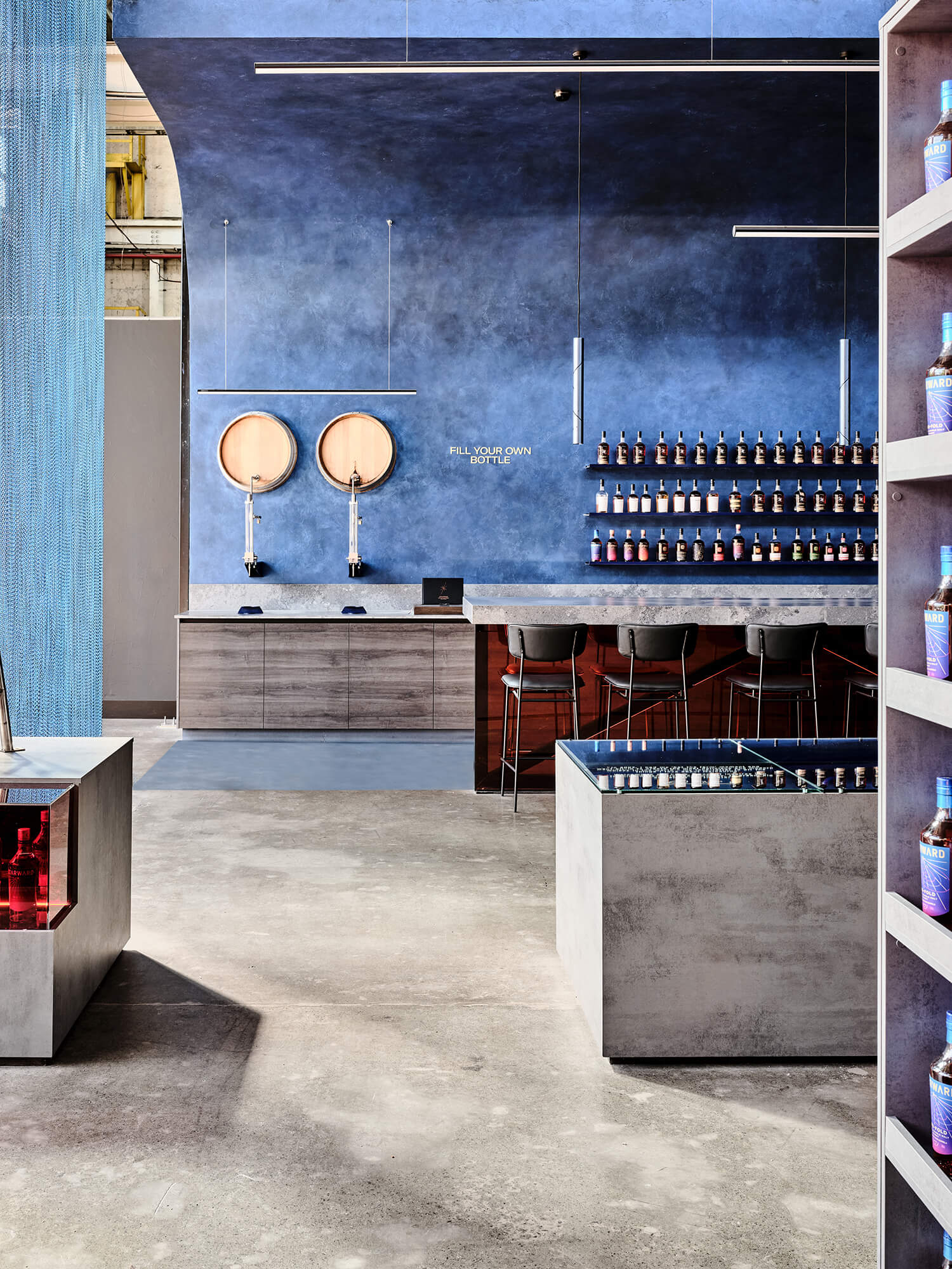 Wall-Mounted Oak Barrels Cobalt Stucco Niche Concrete Plinths Fill Your Own Bottle Station Linear LED Lighting Distillery Retail Area in Starward. Photo by James Geer.