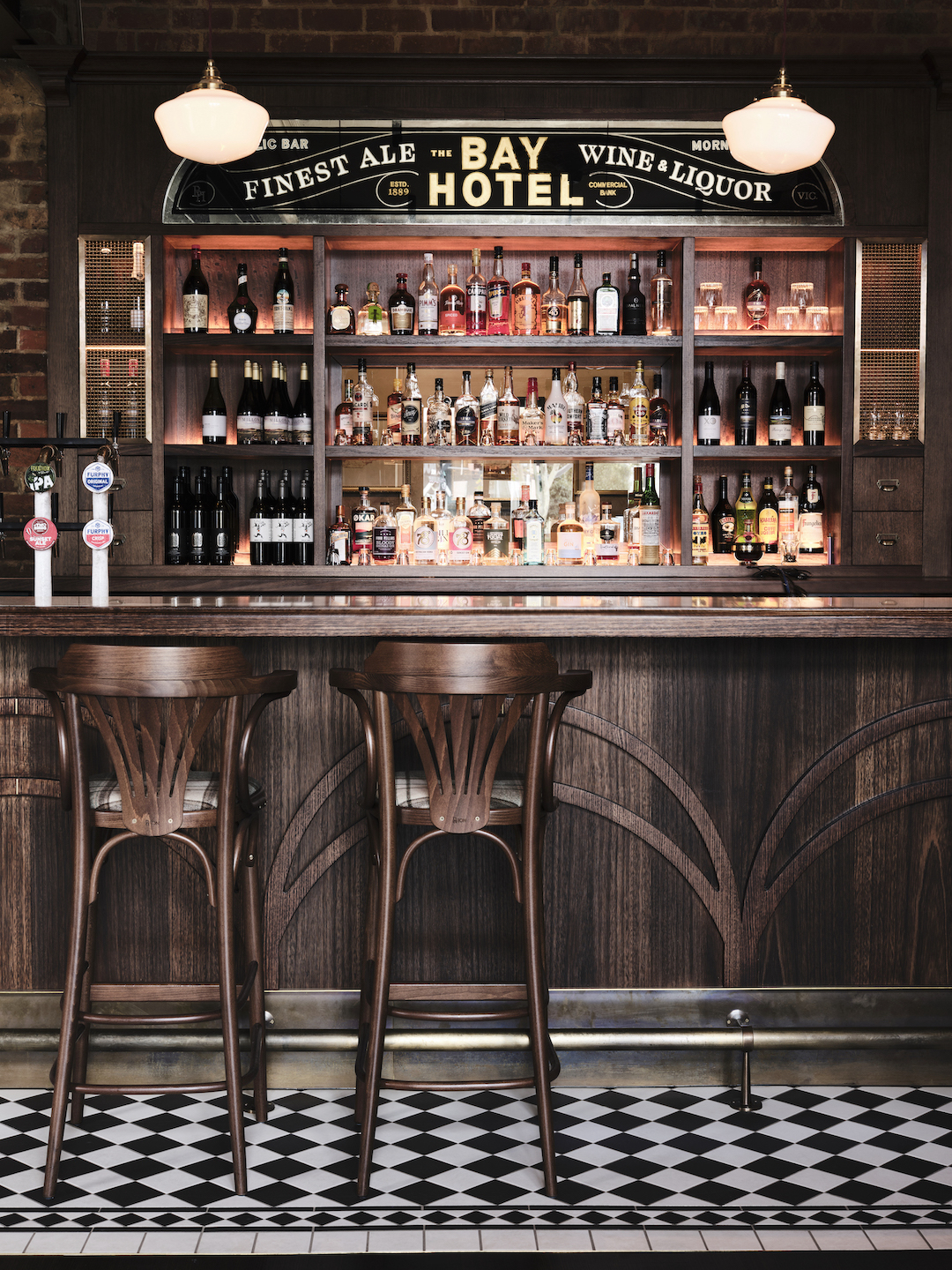Symmetry in Heritage Design Frontal Timber Bar Gold Leaf Mirror Signage Illuminated Spirits Display Bentwood Stools Checkerboard Tiles in The Bay Hotel. Photo by James Geer.