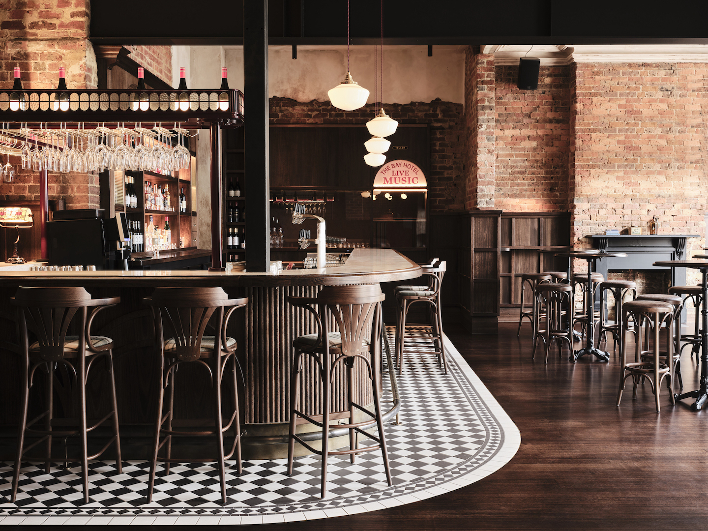 Curved Timber Bar with Checkerboard Tiling Bentwood Stools Exposed Brick Heritage Fireplace and Neon Signage Detail in The Bay Hotel. Photo by James Geer.