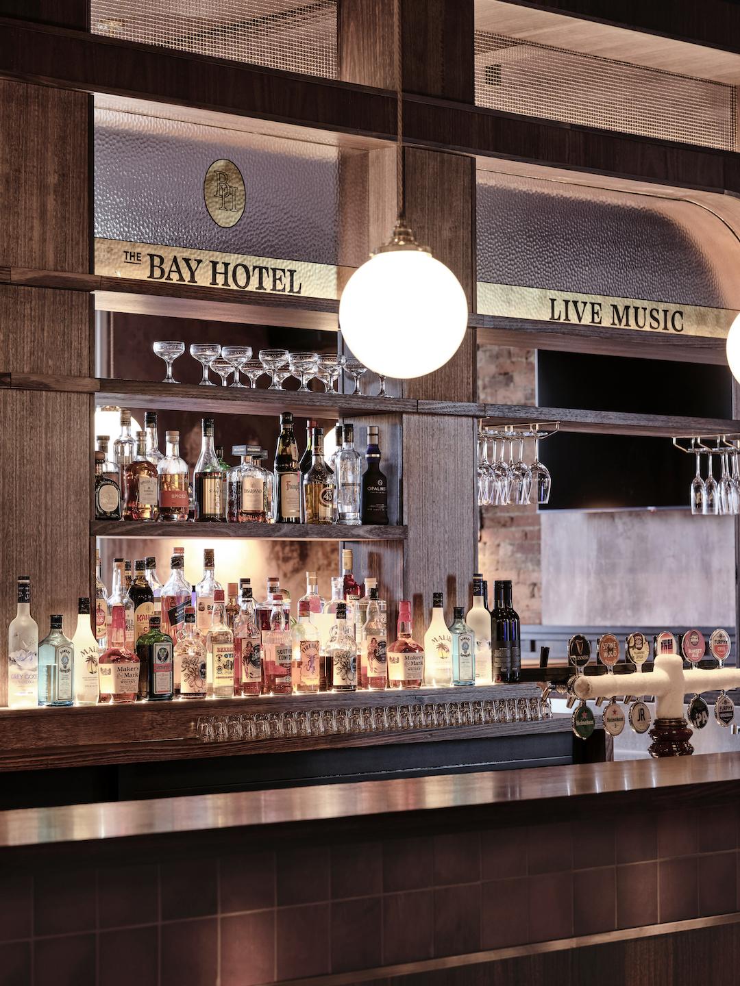 Backlit Spirits Shelving with Gold Leaf Glass Signage Globe Pendant Light Tiled Counter Front and Beer Taps Heritage Venue Style in The Bay Hotel. Photo by James Geer.