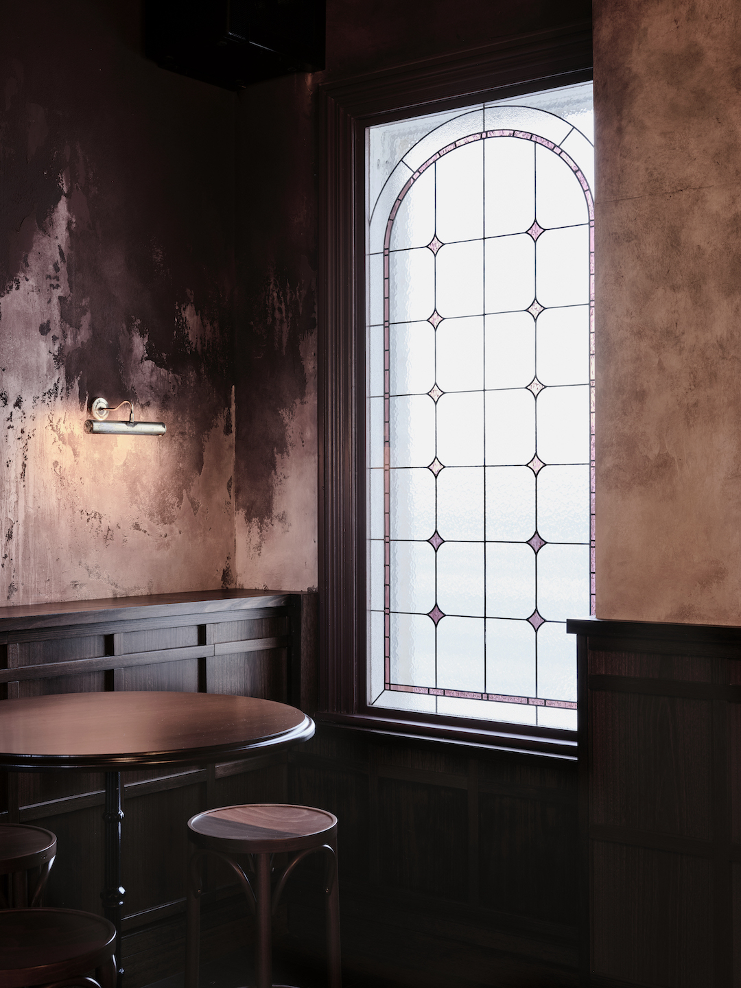 Arched Leadlight Glazing with Pink Diamond Accents Walnut Wainscotting Round Timber Pedestal Table and Brass Sconce in The Bay Hotel. Photo by James Geer.