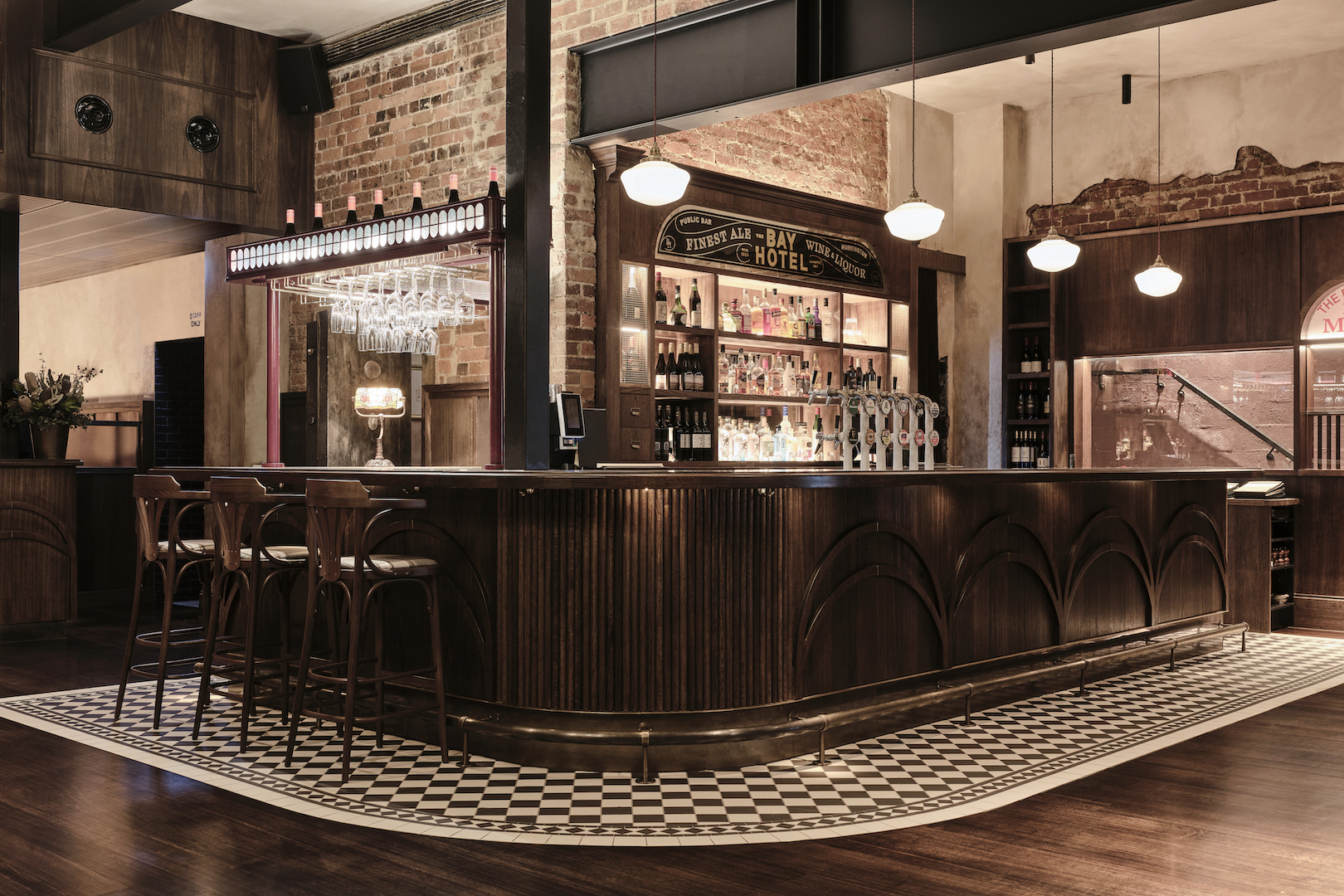 Ornate Dark Timber Counters with Fluted Detailing Checkerboard Tile Border Bentwood Stools Exposed Masonry and Heritage Signage in The Bay Hotel. Photo by James Geer.