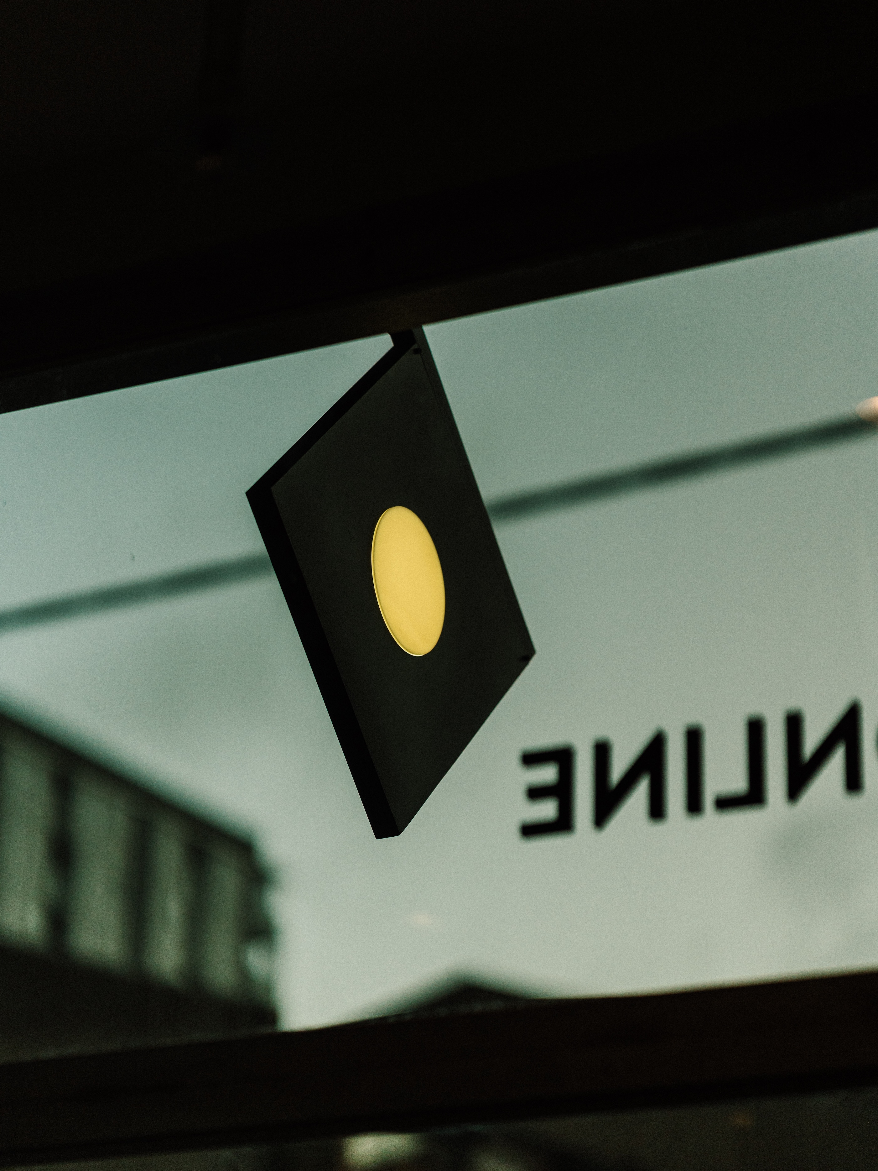 Close-Up of Diamond Blade Sign with Illuminated Circular Logo Against Glass Window and Industrial Urban Backdrop in The Local Drop. Photo by Pier Carthew and Kevin McDowell.