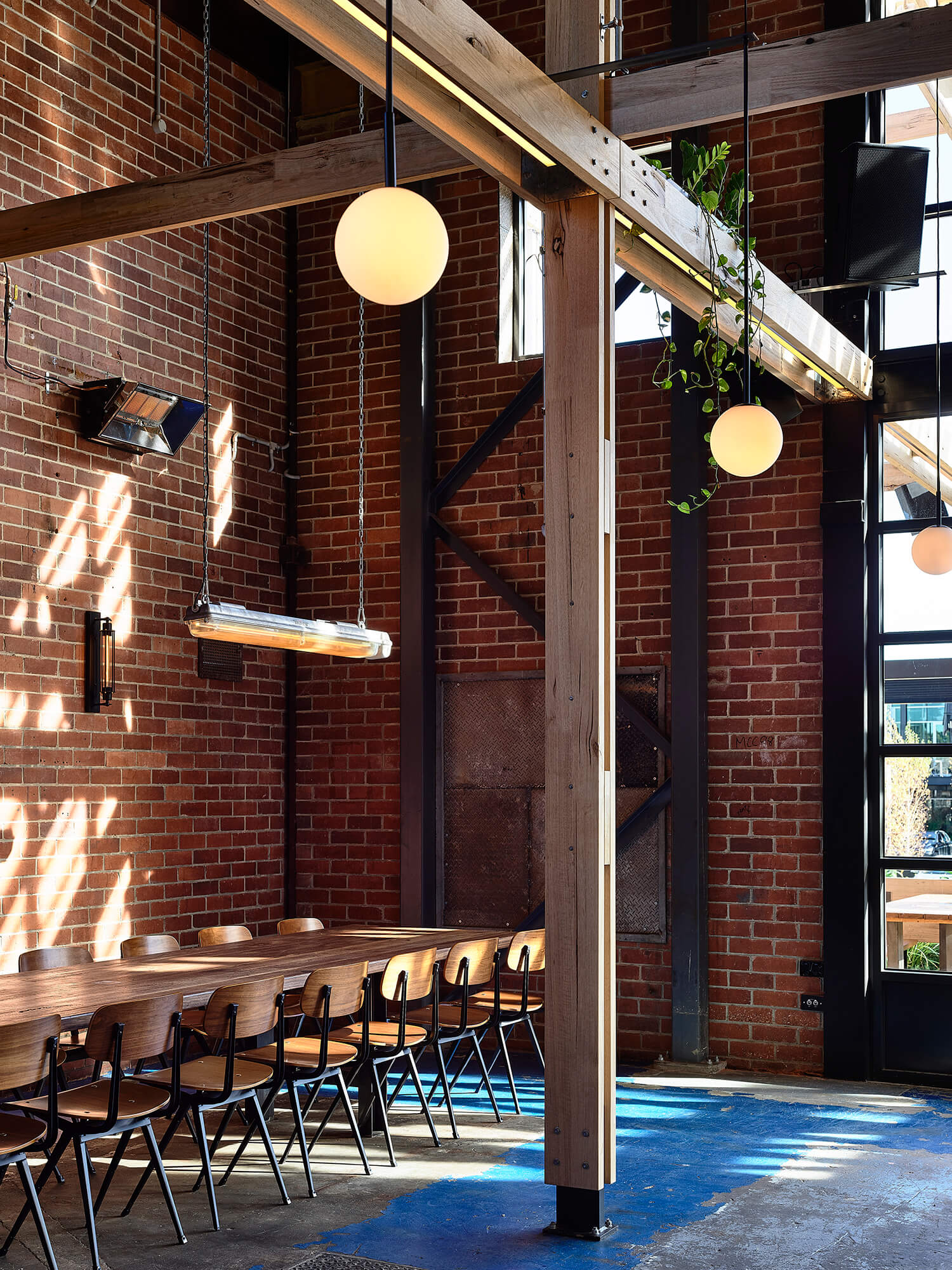 Industrial Dining Space with Exposed Brick Timber Beams Globe Pendent Lighting Long Communal Table and Blue Floor Accents in Stomping Ground Morris Moor. Photo by Derek Swalwell.