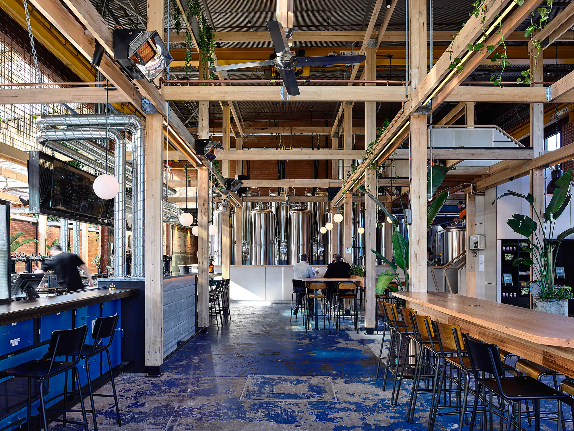 Expansive Brewpub Interior with Timber Post-and-Beam Structure Stainless Steel Vats Blue Patina Floors and Industrial Lighting in Stomping Ground Morris Moor. Photo by Derek Swalwell.