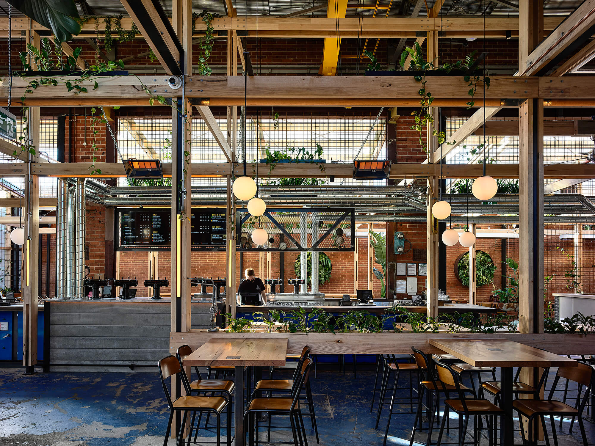 Industrial Dining Area with Timber Post-and-Beam Structure Globe Pendants Integrated Greenery and Blue Patina Floors in Stomping Ground Morris Moor. Photo by Derek Swalwell.