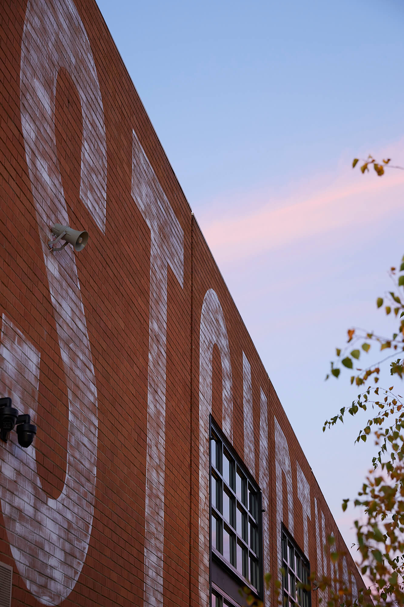 Large Scale Painted Brick Signage on Industrial Facade with PA Speaker and Sunset Sky Backdrop at Stomping Ground Morris Moor. Photo by Derek Swalwell.
