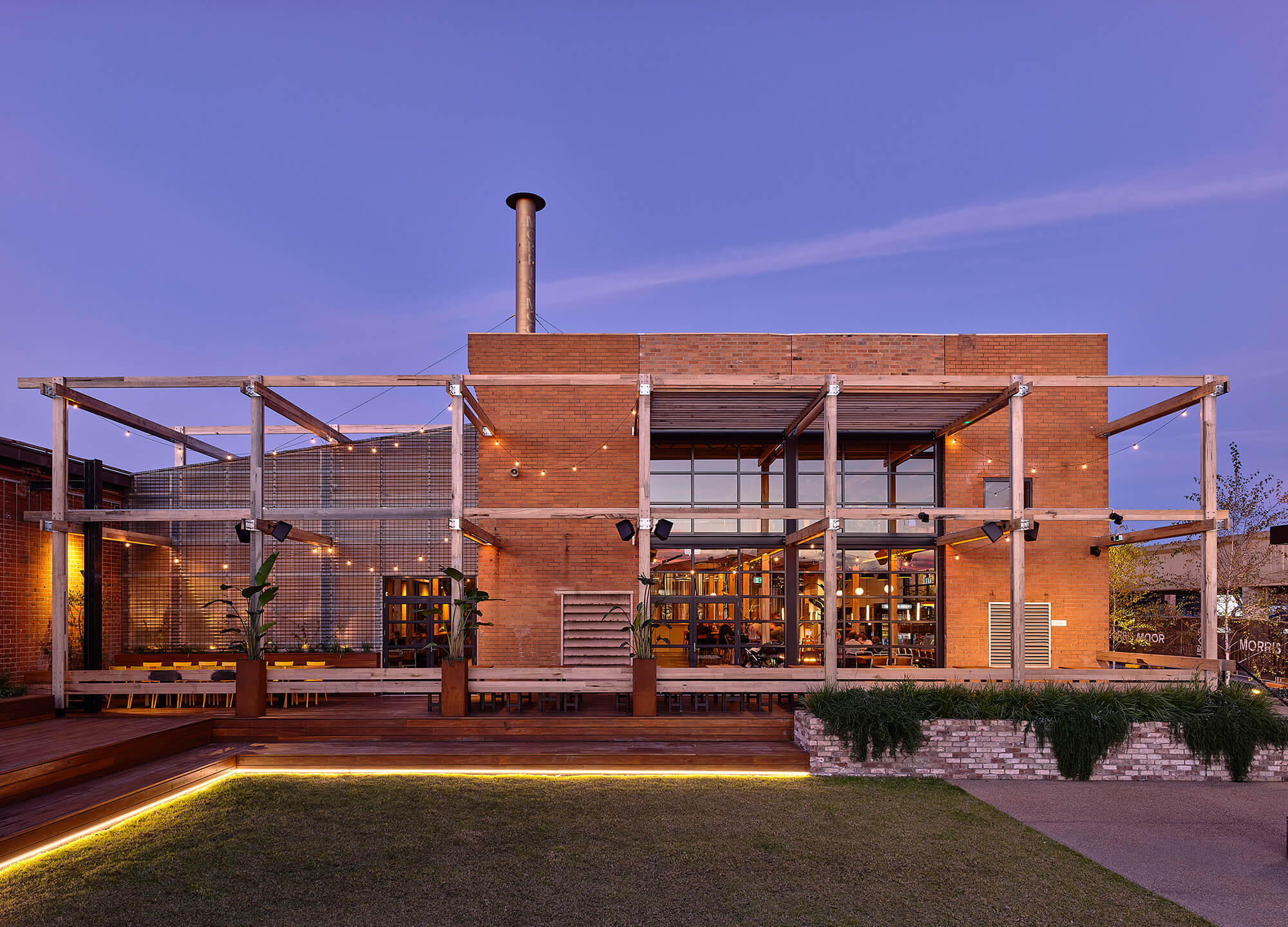 Industrial Outdoor Terrace with Timber Pergola Festoon Lighting Brick Facade Large Glass Windows and Grassy Courtyard at Stomping Ground Morris Moor. Photo by Derek Swalwell.