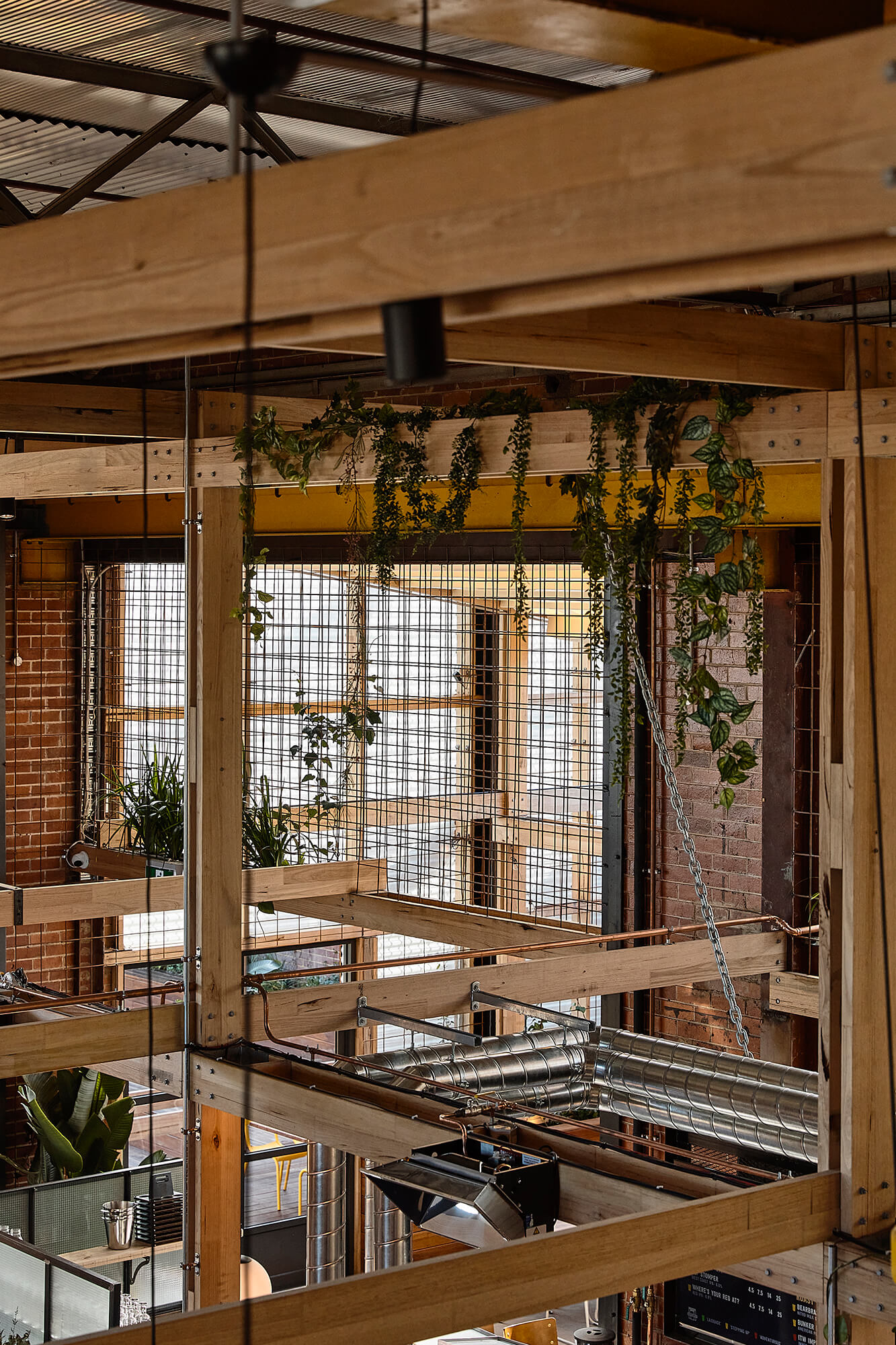 Intricate Timber Post-and-Beam Ceiling Structure with Hanging Greenery Steel Mesh Screens Industrial Ducting and Brick Walls at Stomping Ground Morris Moor. Photo by Derek Swalwell.
