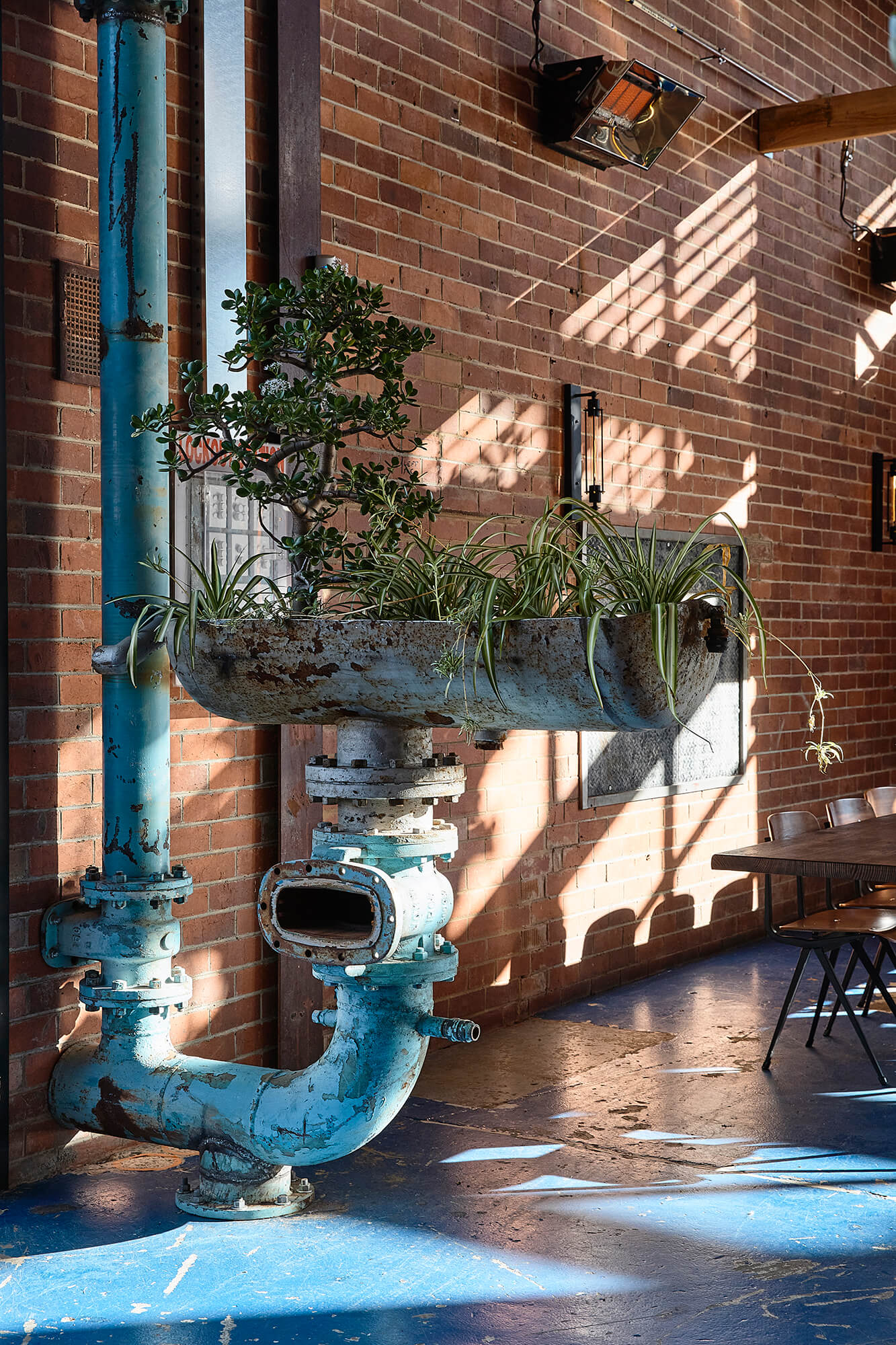Repurposed Industrial Blue Pipe Planter with Lush Greenery Mounted on Exposed Brick Wall with Blue Patina Floors in Stomping Ground Morris Moor. Photo by Derek Swalwell.