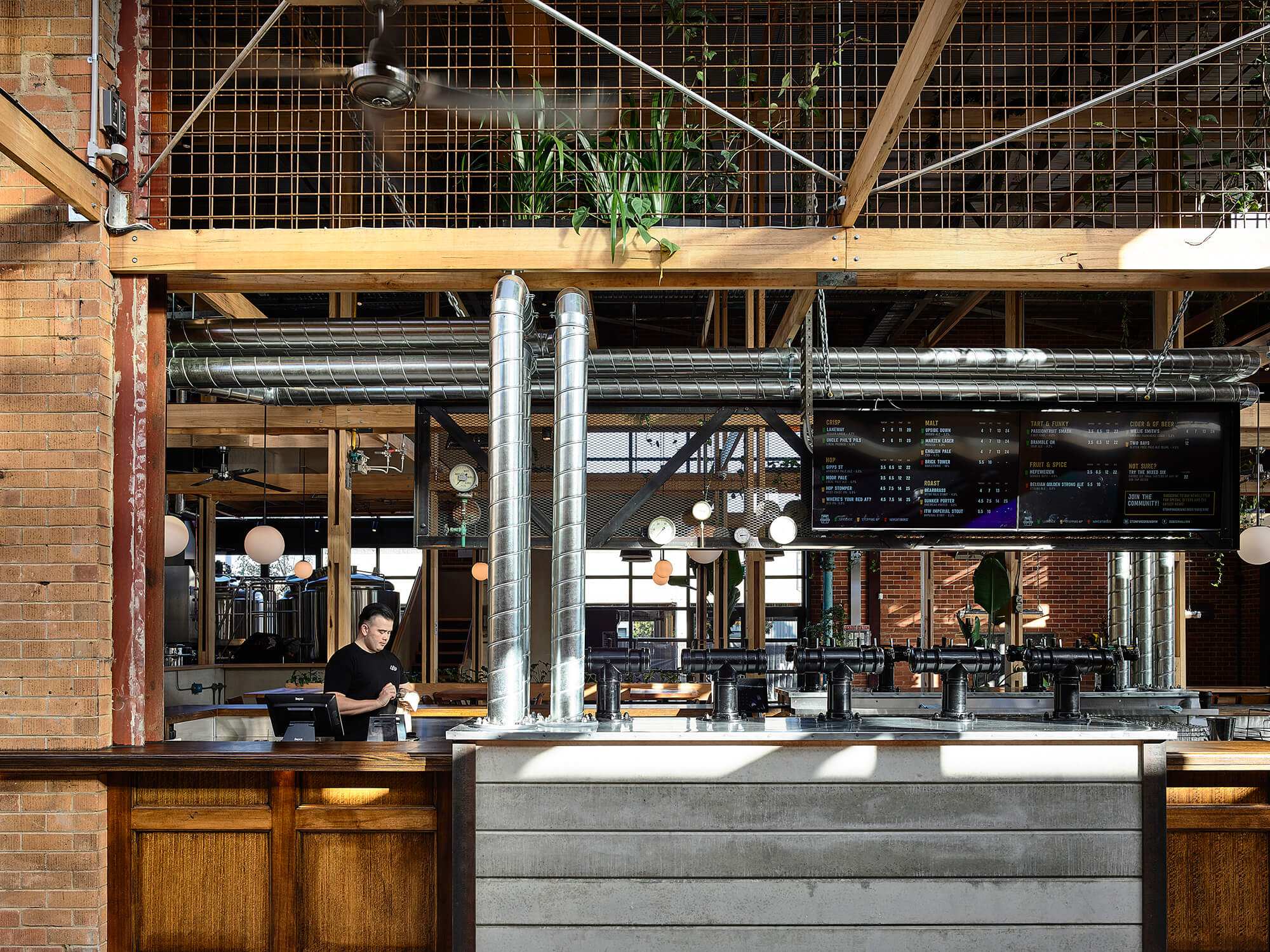 Frontal View of Concrete and Timber Bar with Industrial Beer Taps Exposed Silver Ducting and Mesh Bulkhead at Stomping Ground Morris Moor. Photo by Derek Swalwell.