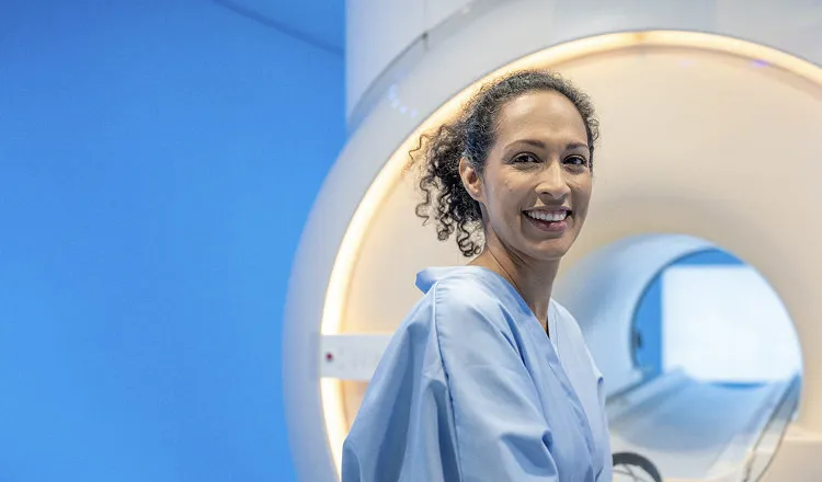 Smiling female technician standing next to MRI machine