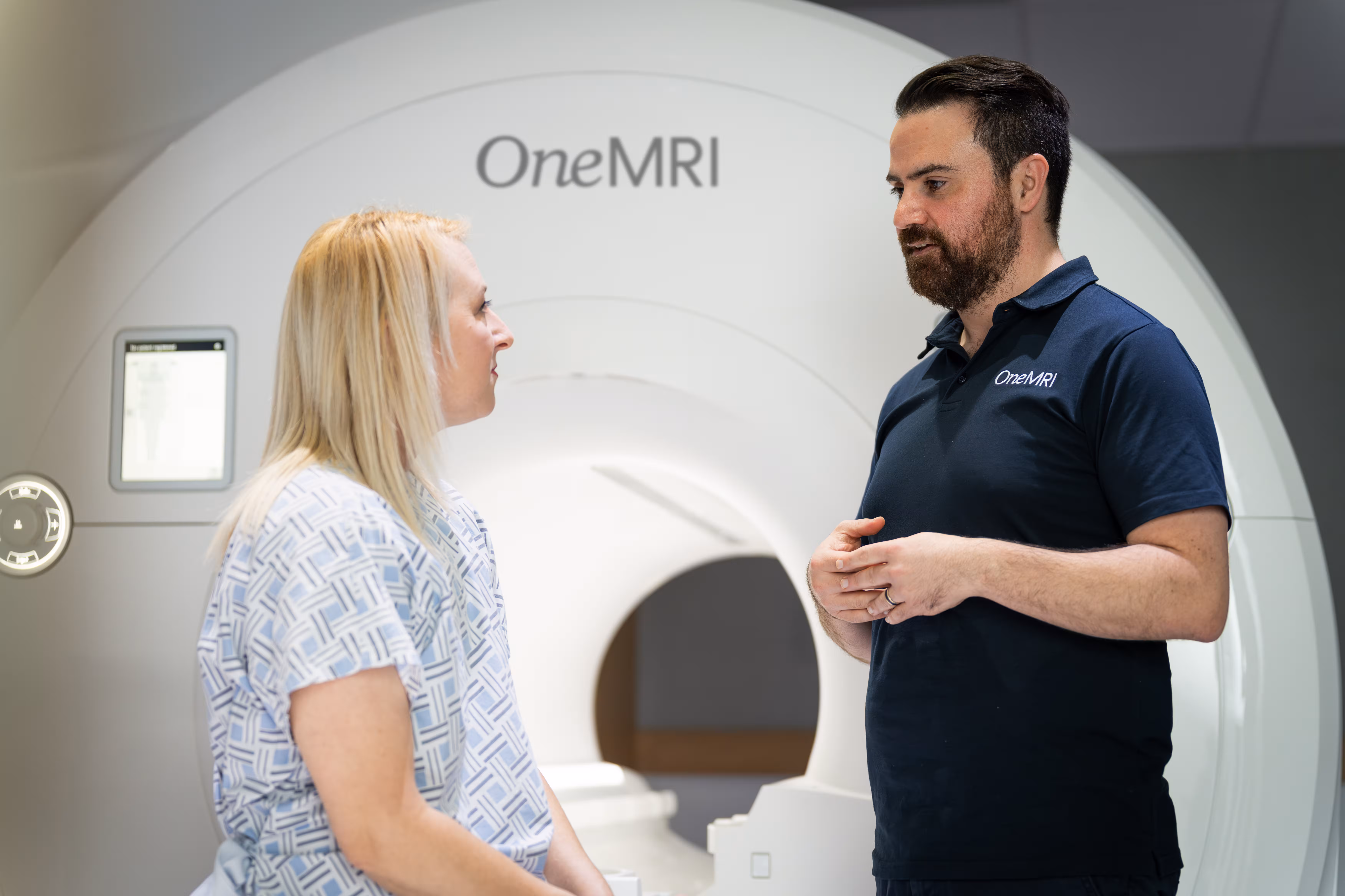 Radiographer talking to patient sitting on an MRI bed