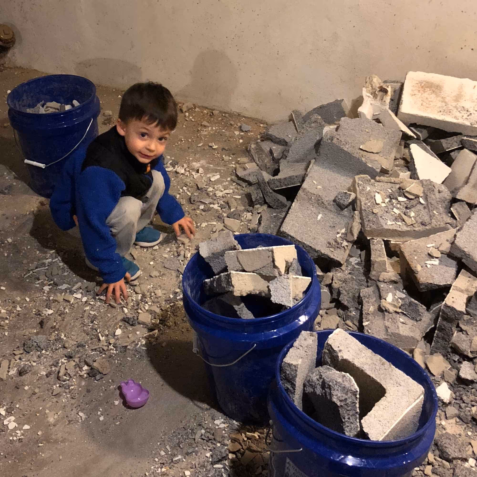 Little boy picking up stone and placing into buckets.