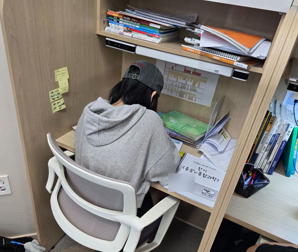 책상 앞에 자기 계획표를 붙여 두고 공부하는 학생의 뒷모습