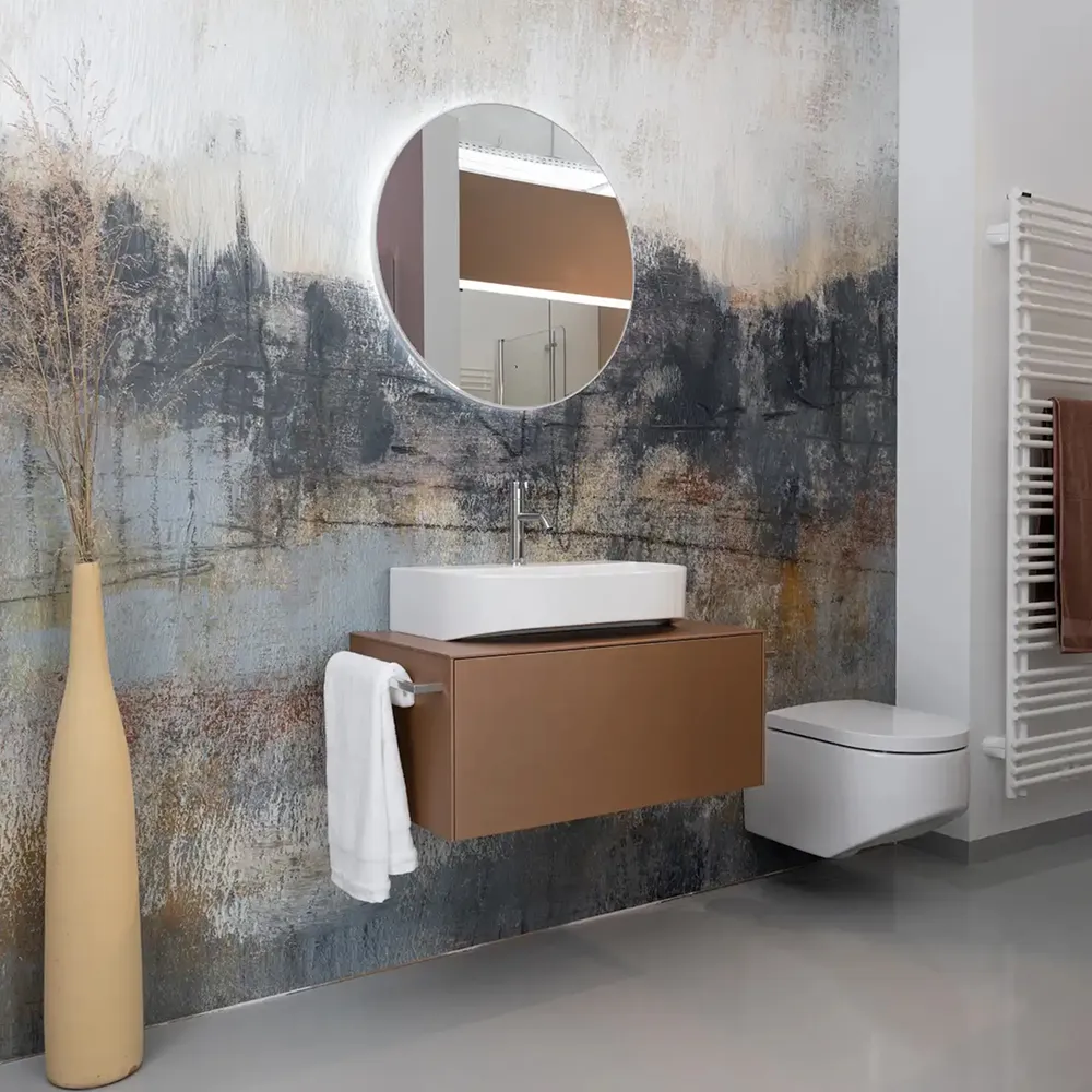 Moderne badeværelse med rundt spejl, væghængt vask og toilet, samt kunstnerisk vægdekoration.