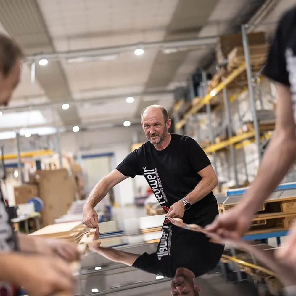 Mand i sort Redwell t-shirt udfører kvalitetskontrol på et spejlvarmer i en fabrik.