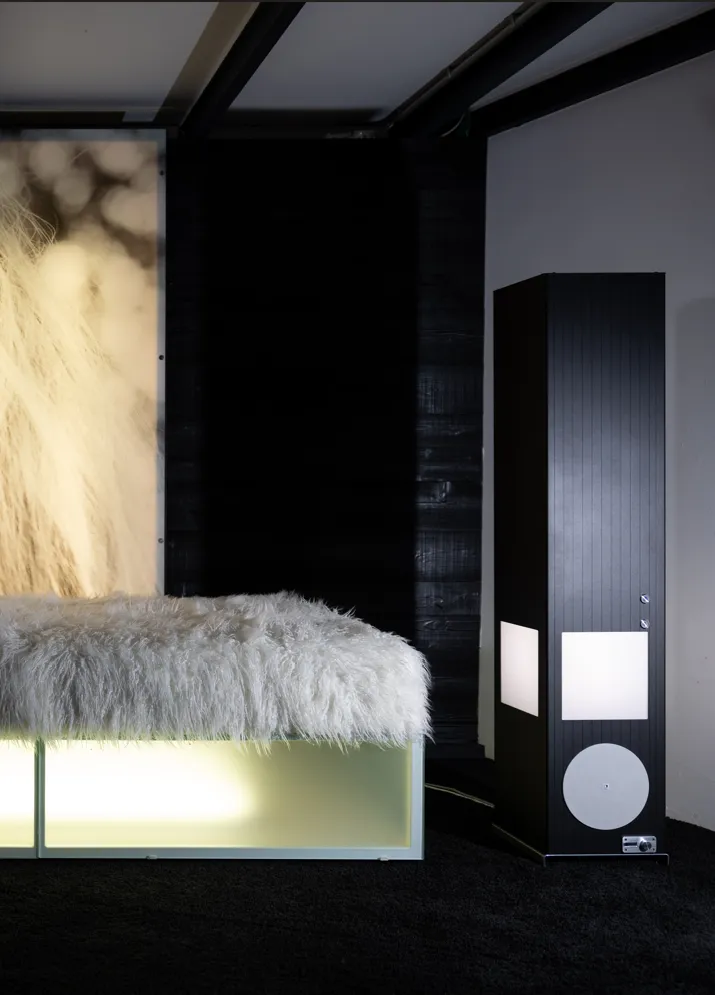 Høj, fritstående Redwell Tower infrarød varmesøjle i sort design. Varmesøjlen er placeret på gulvet i en moderne, mørk hjemmebiograf ved siden af en oplyst sofa, hvor den giver jævn og behagelig opvarmning i rummet.