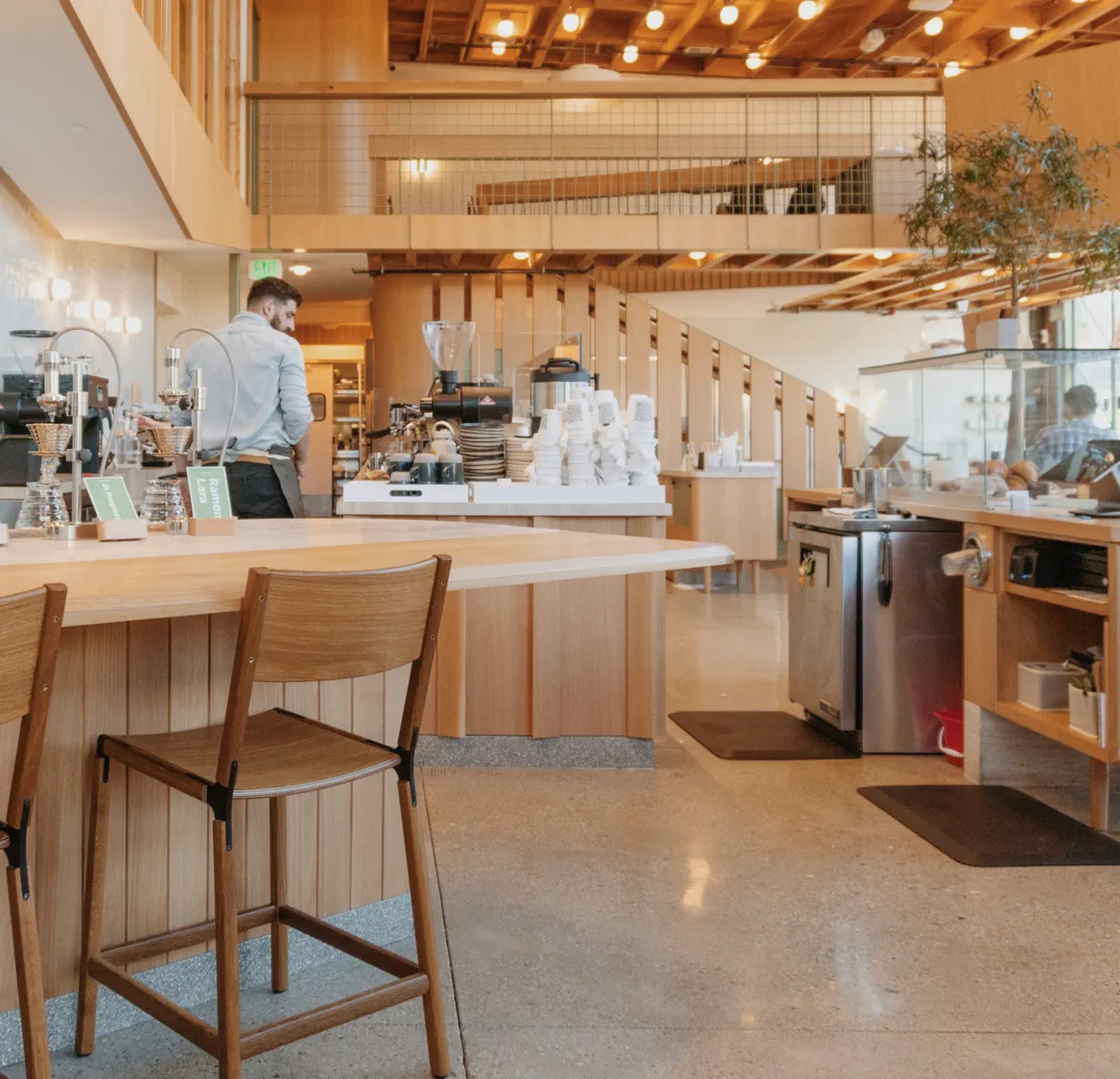 Hvide Redwell infrarøde varmepaneler diskret indbygget i træloftet i en moderne café eller kantine. Viser en æstetisk og pladsbesparende opvarmningsløsning til store erhvervslokaler.