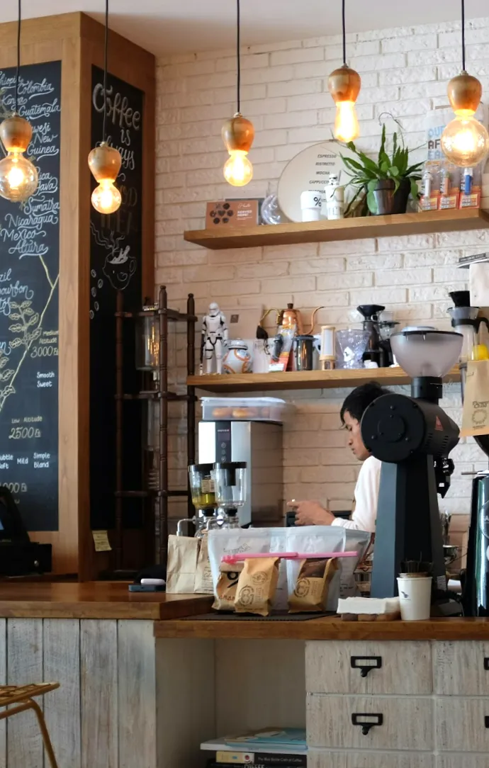 Hvide Redwell WE-Line infrarøde varmepaneler monteret diskret i loftet i en hyggelig kaffebar med rustik murstensvæg, træhylder og varme pendellamper.