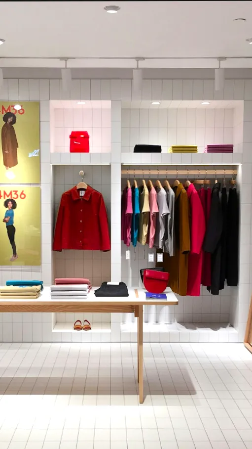 Hvide Redwell WE-Line infrarøde varmepaneler integreret diskret i loftet i en lyst indrettet tøjbutik med tøjreoler og udstillingsborde. Viser pladsbesparende opvarmning til butiksmiljøer.