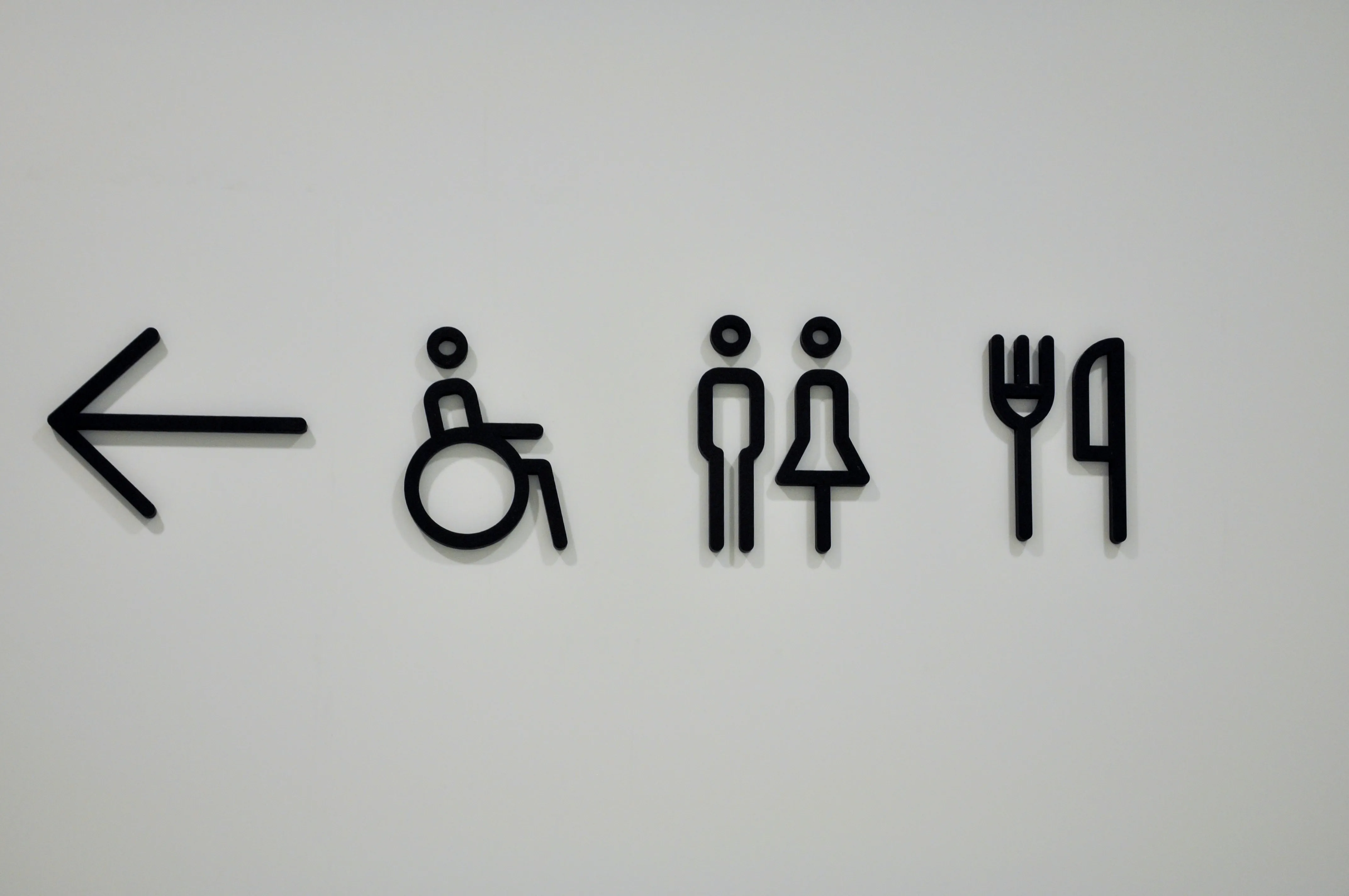 Hvidt Redwell infrarødt glasskilt med varme trykt med sorte piktogrammer for handicap, toilet og restaurant. Viser funktionel skiltning med integreret infrarød opvarmning til erhverv og offentlige lokaler.