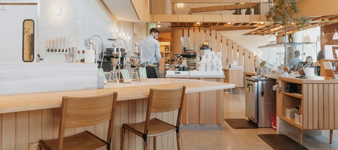 Hvide Redwell infrarøde varmepaneler diskret indbygget i træloftet i en moderne café eller kantine. Viser en æstetisk og pladsbesparende opvarmningsløsning til store erhvervslokaler.