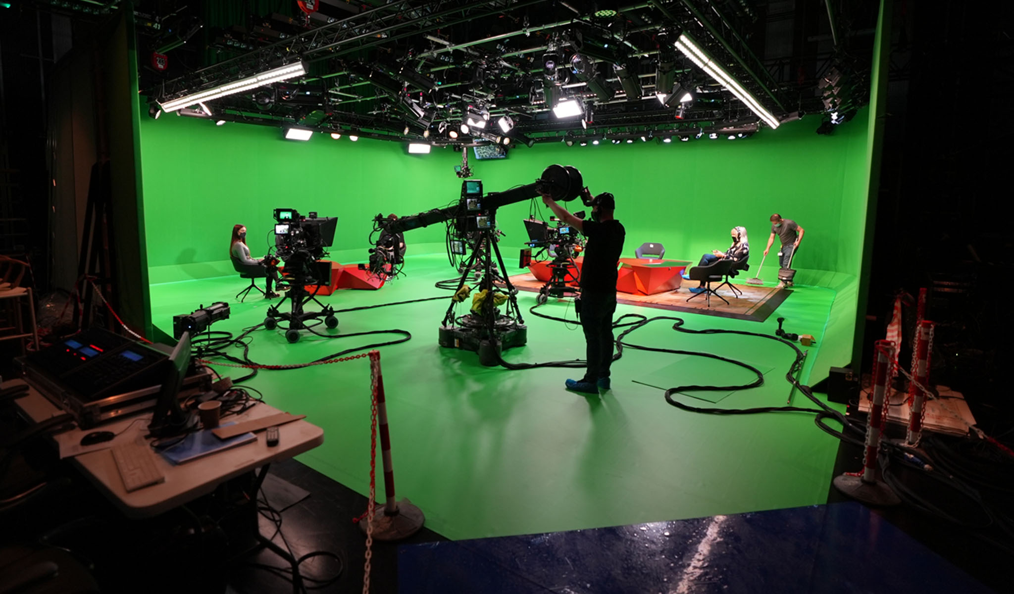 TV studio green screen set with cameras, crew, and two seated people during production.